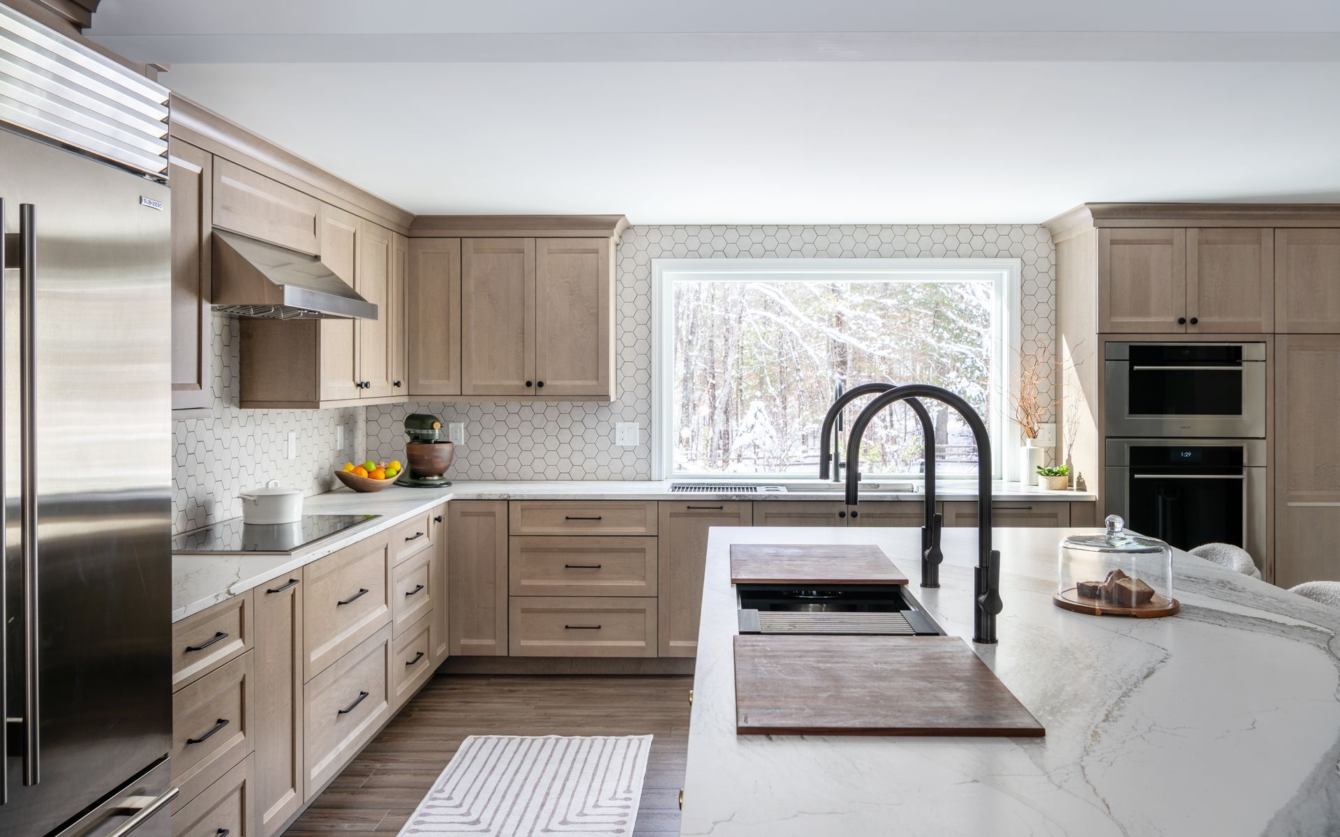 Modern kitchen with light wood cabinets, white island, stainless appliances, and a window over the sink