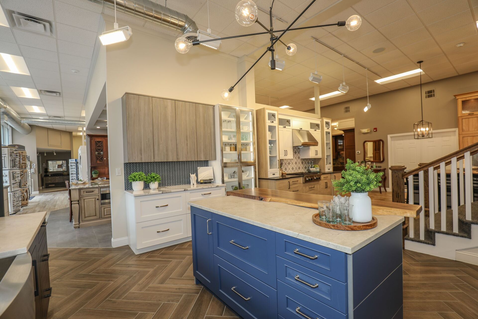 Modern kitchen showroom with blue island, white cabinets, wood flooring, and pendant lights