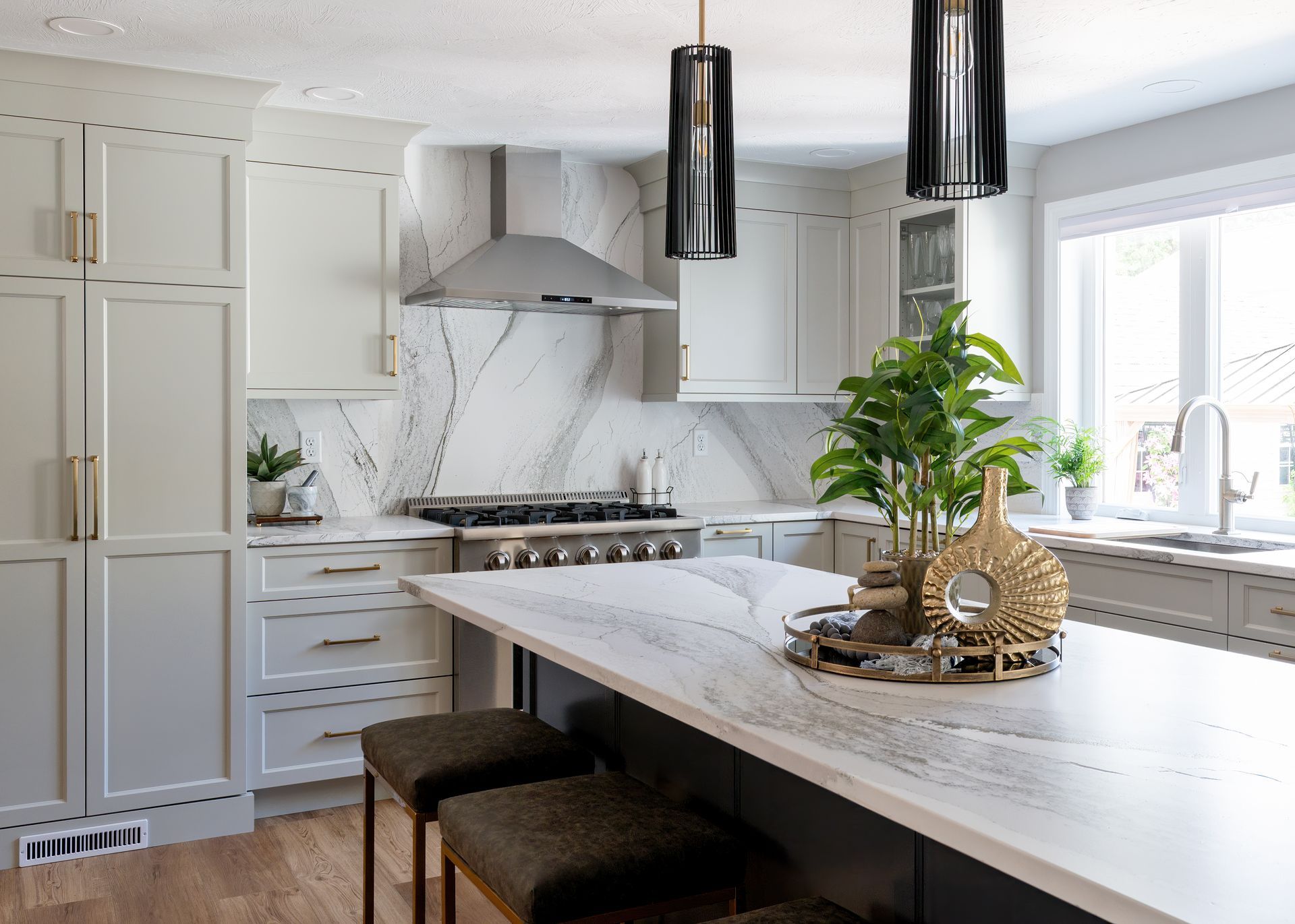Bright modern kitchen with white cabinets, marble island, pendant lights, and a potted plant by the window