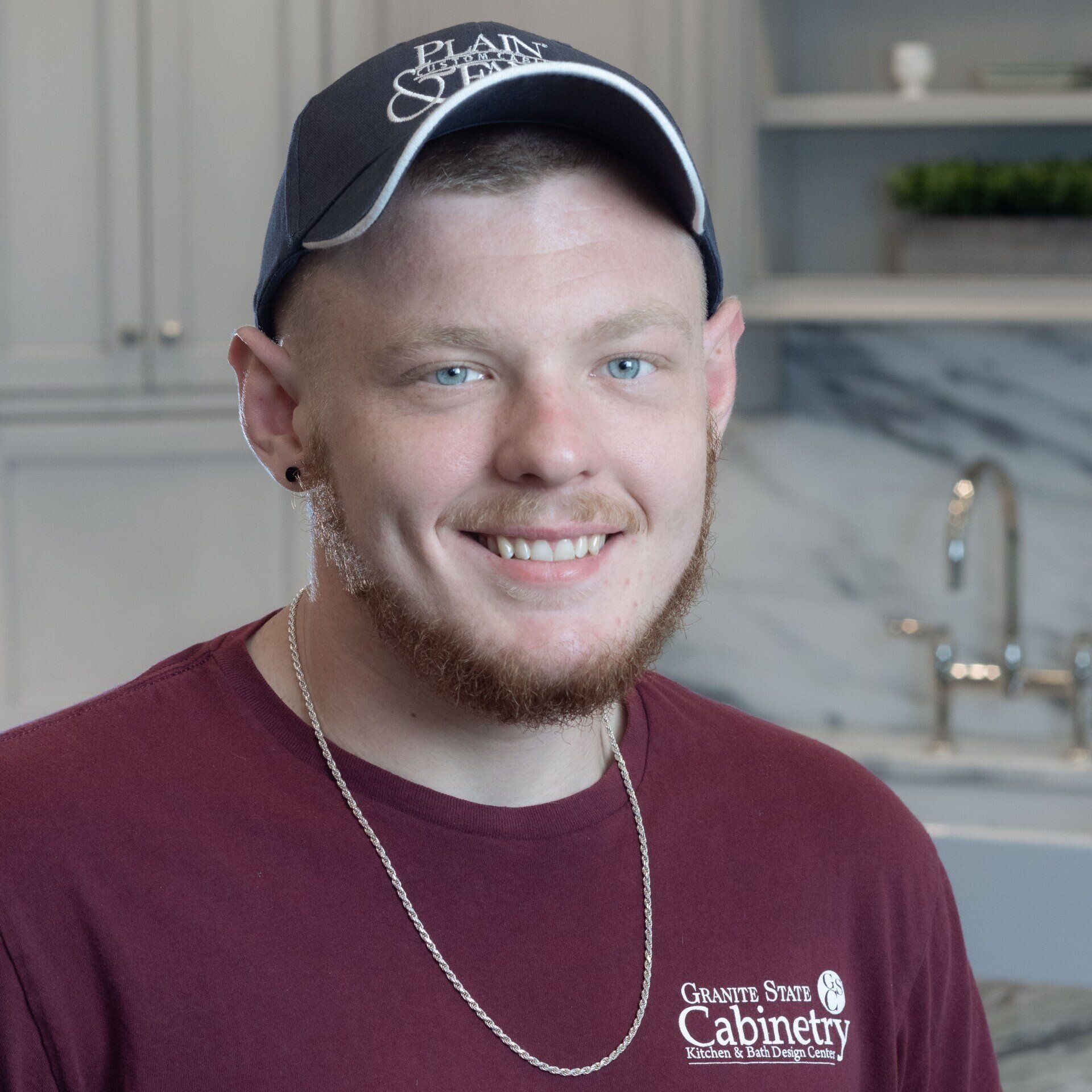 Smiling person in a black cap and maroon shirt in a bright kitchen