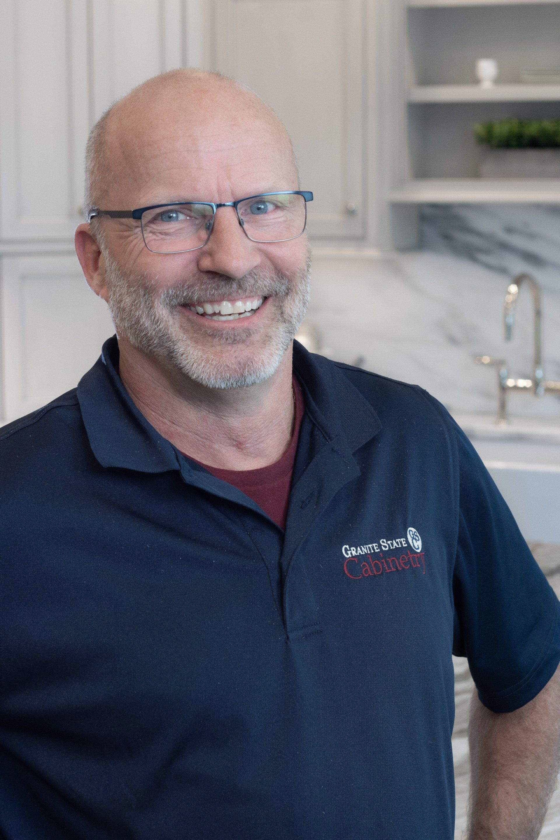 Smiling man in a navy polo shirt standing in a bright kitchen with marble countertops