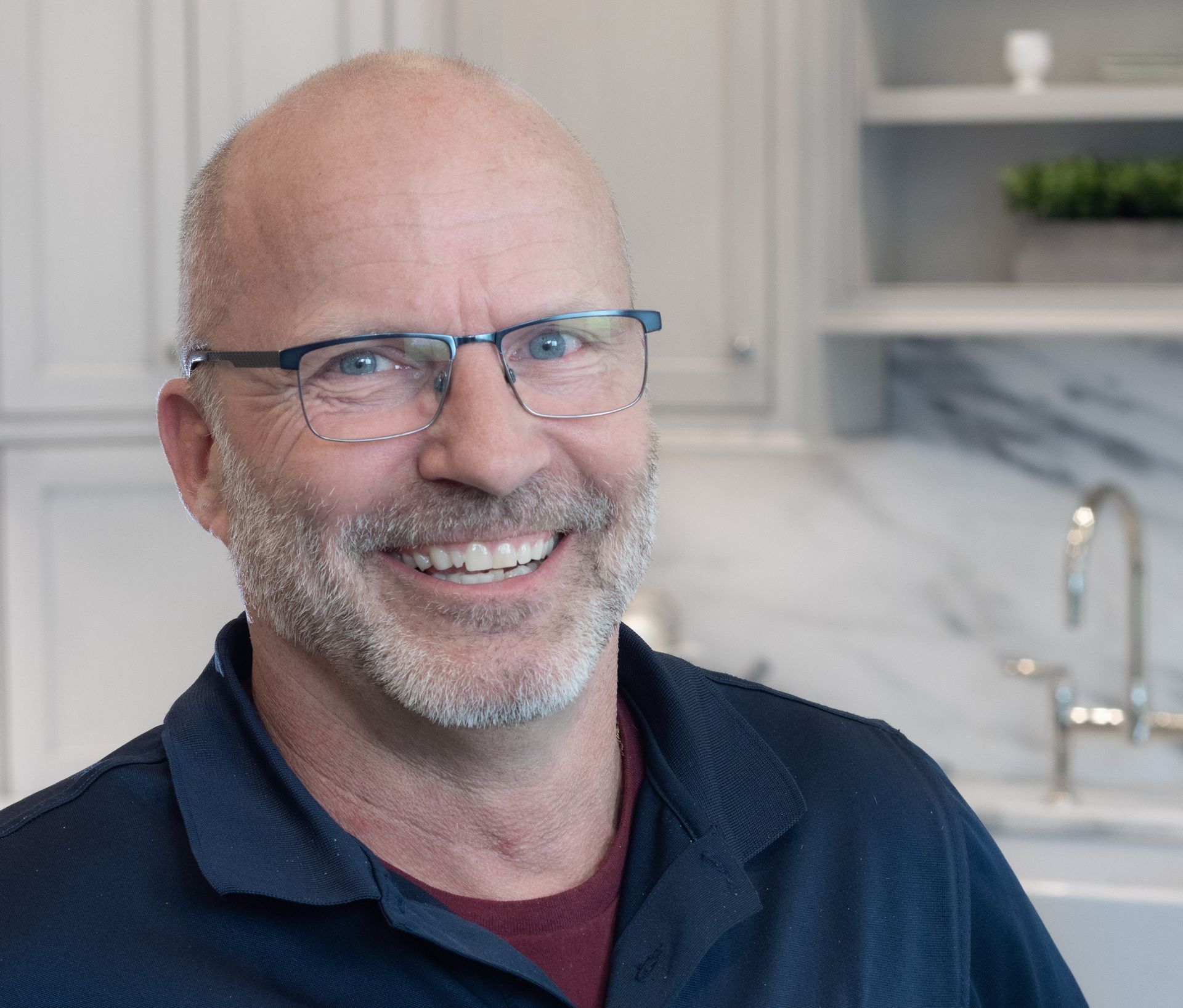 Smiling bald man with glasses in a navy shirt in a bright kitchen