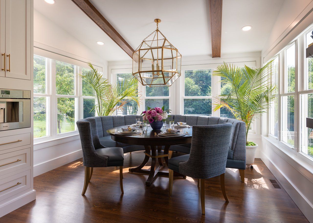 Bright dining room with round table, dark chairs, hardwood floor, large windows, and a gold chandelier.
