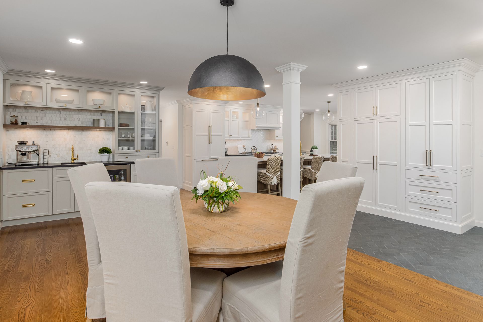 Bright white open-plan kitchen and dining area with round wooden table and black pendant light