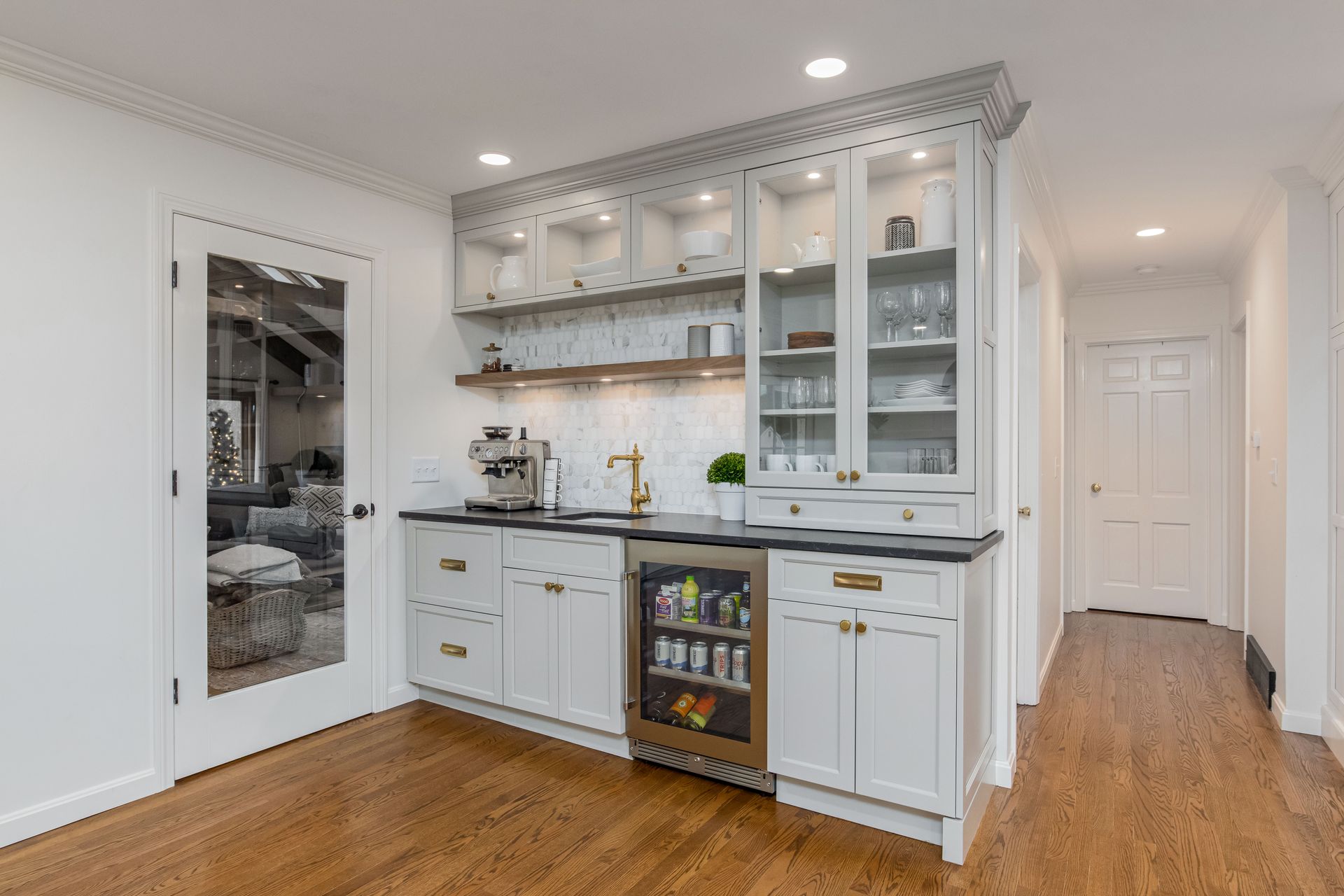 Bright white kitchen with glass cabinets, dark countertops, wood floor, and a small hallway.
