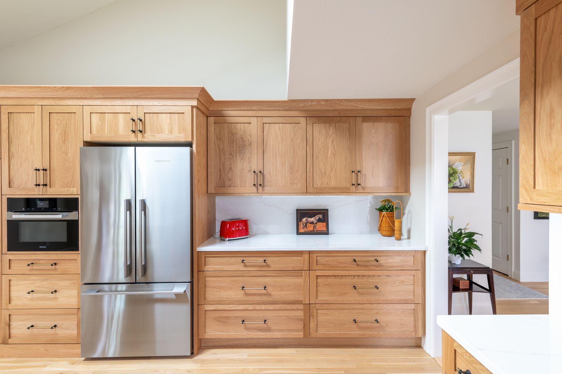 Modern kitchen with light wood cabinets, stainless steel refrigerator, and a white countertop