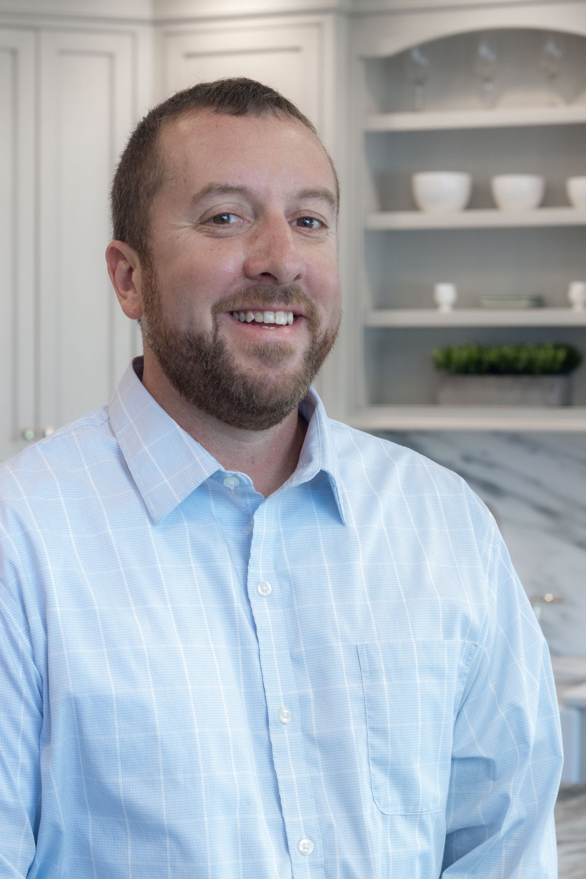 Smiling man in a light blue shirt standing in a bright kitchen with white cabinets and shelves