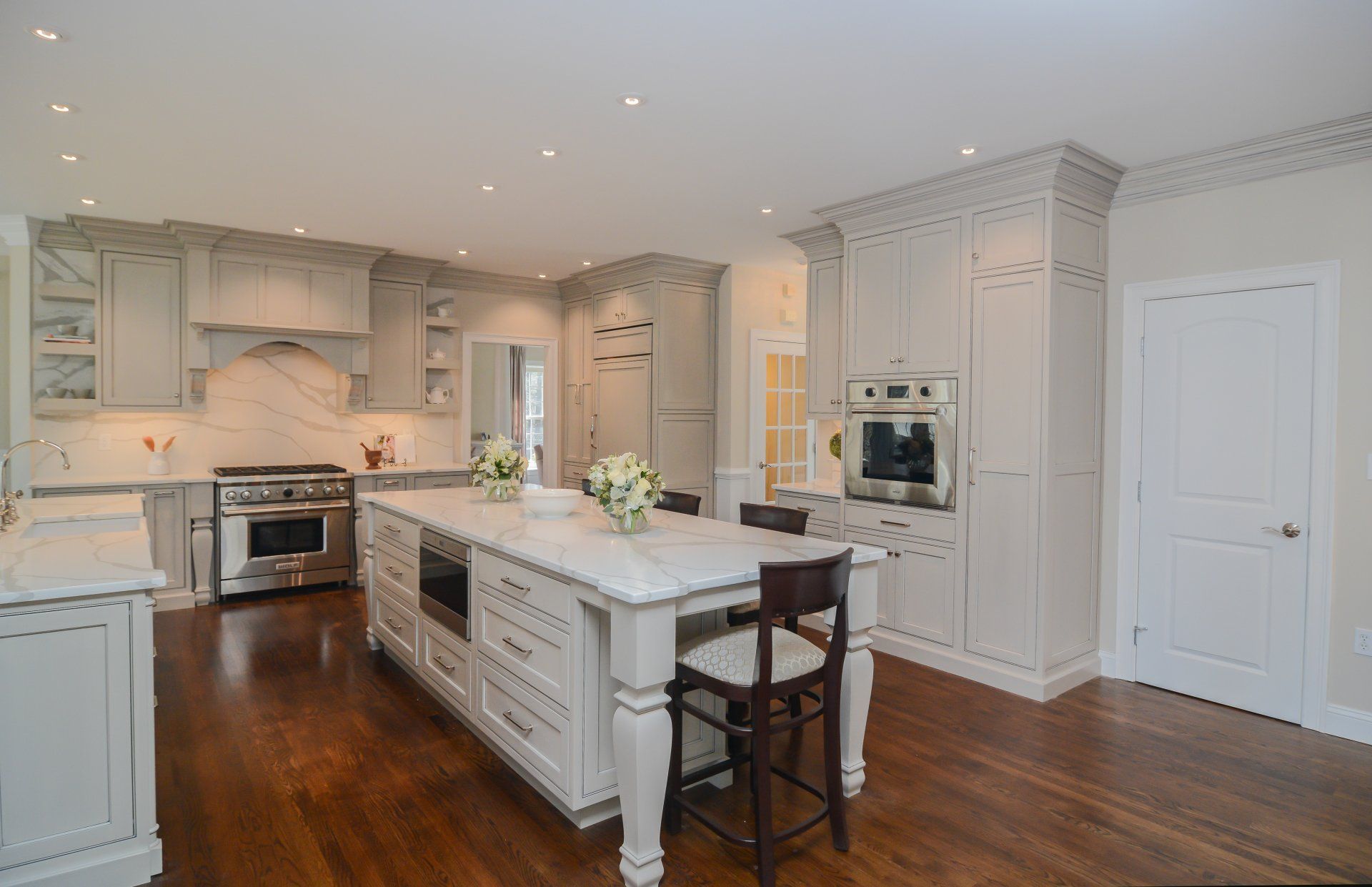 Bright white kitchen with marble island, dark wood floors, and stainless steel appliances