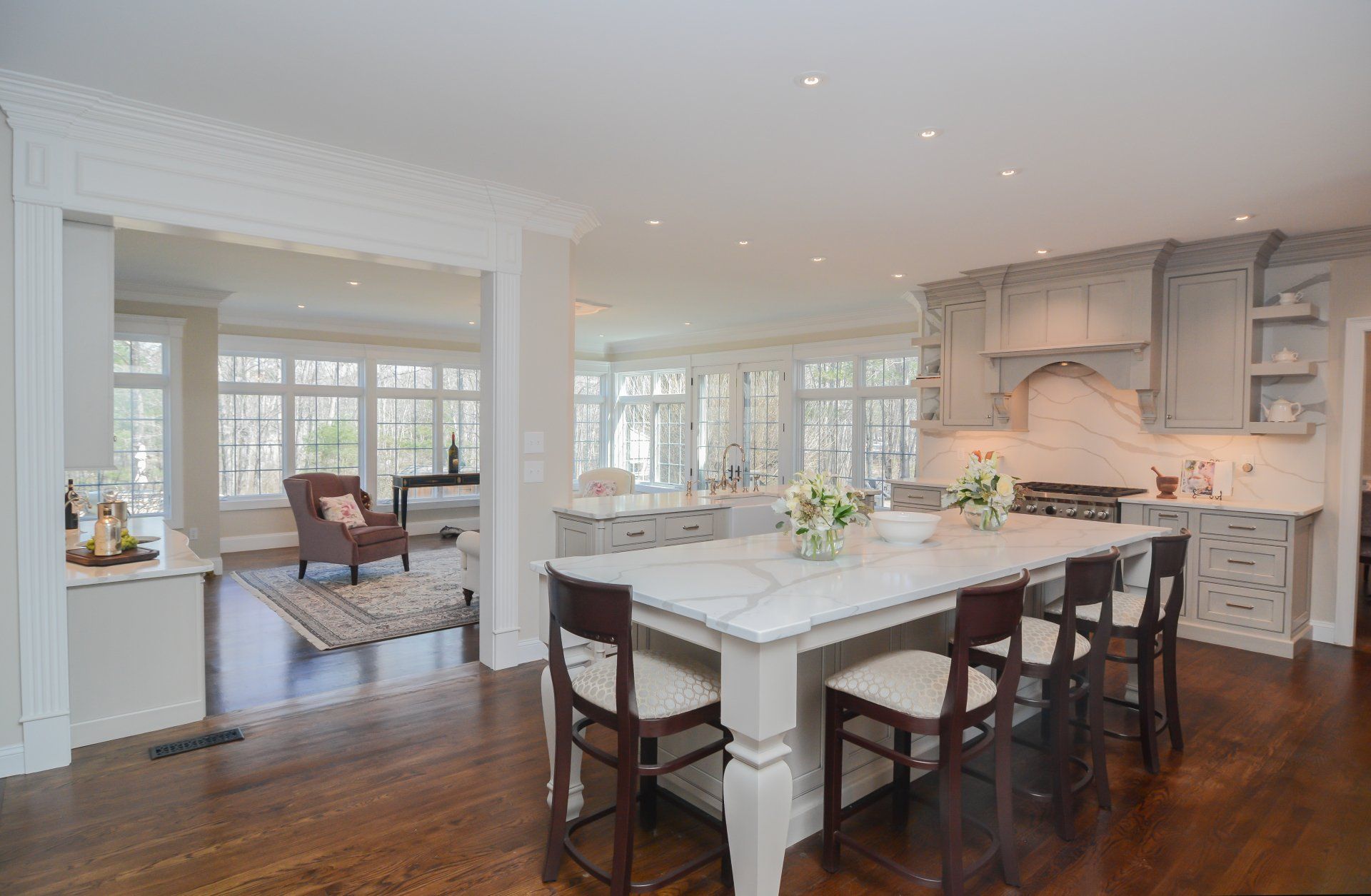 Bright open kitchen with white island, dark wood floors, and breakfast nook near large windows.
