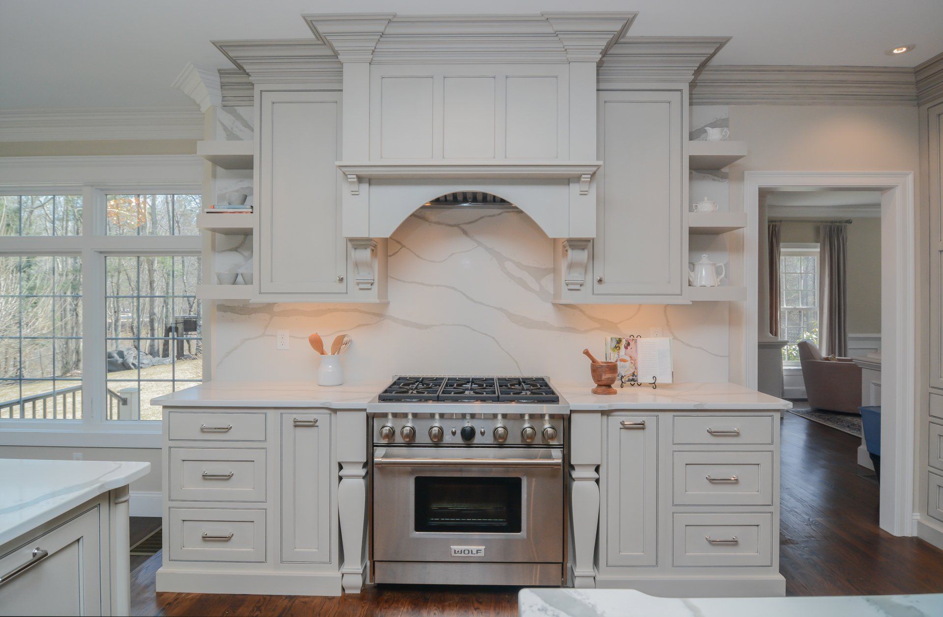Bright white kitchen with a stainless steel stove, custom range hood, and hardwood floors