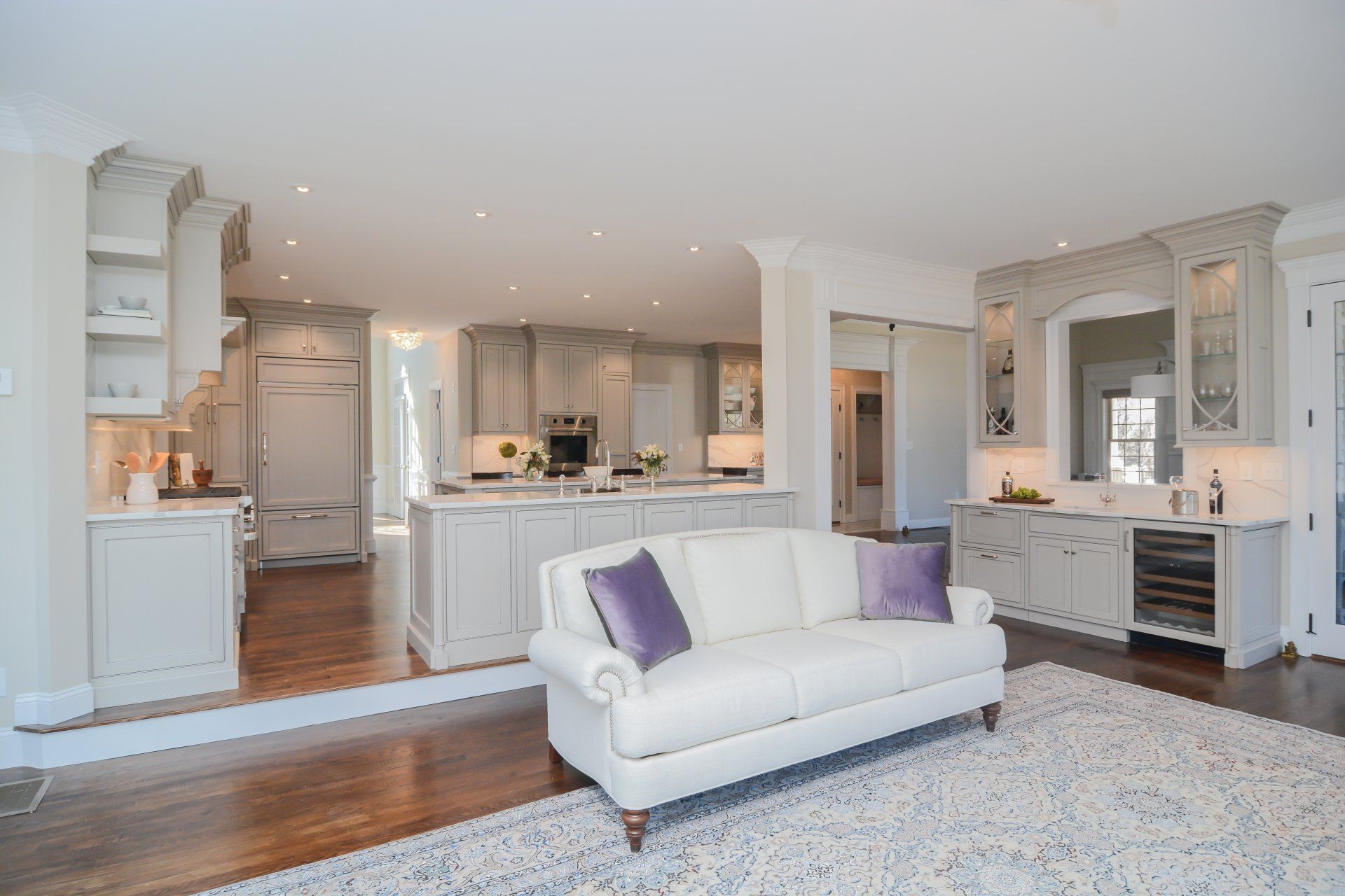 Bright open-plan kitchen and living room with white cabinets, gray sofa, and large patterned rug