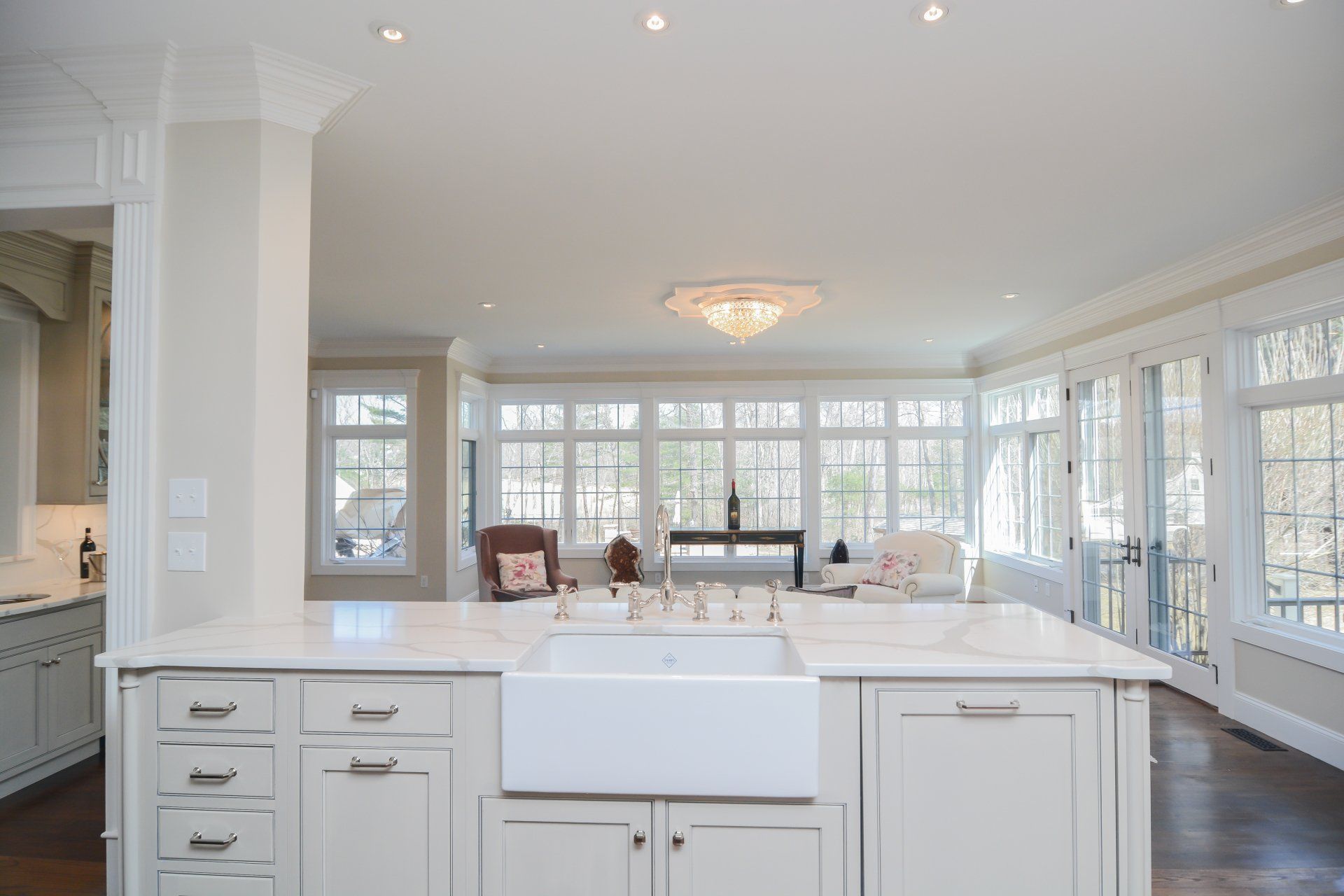 Bright white kitchen opening to a sunlit living room with large windows and a central island
