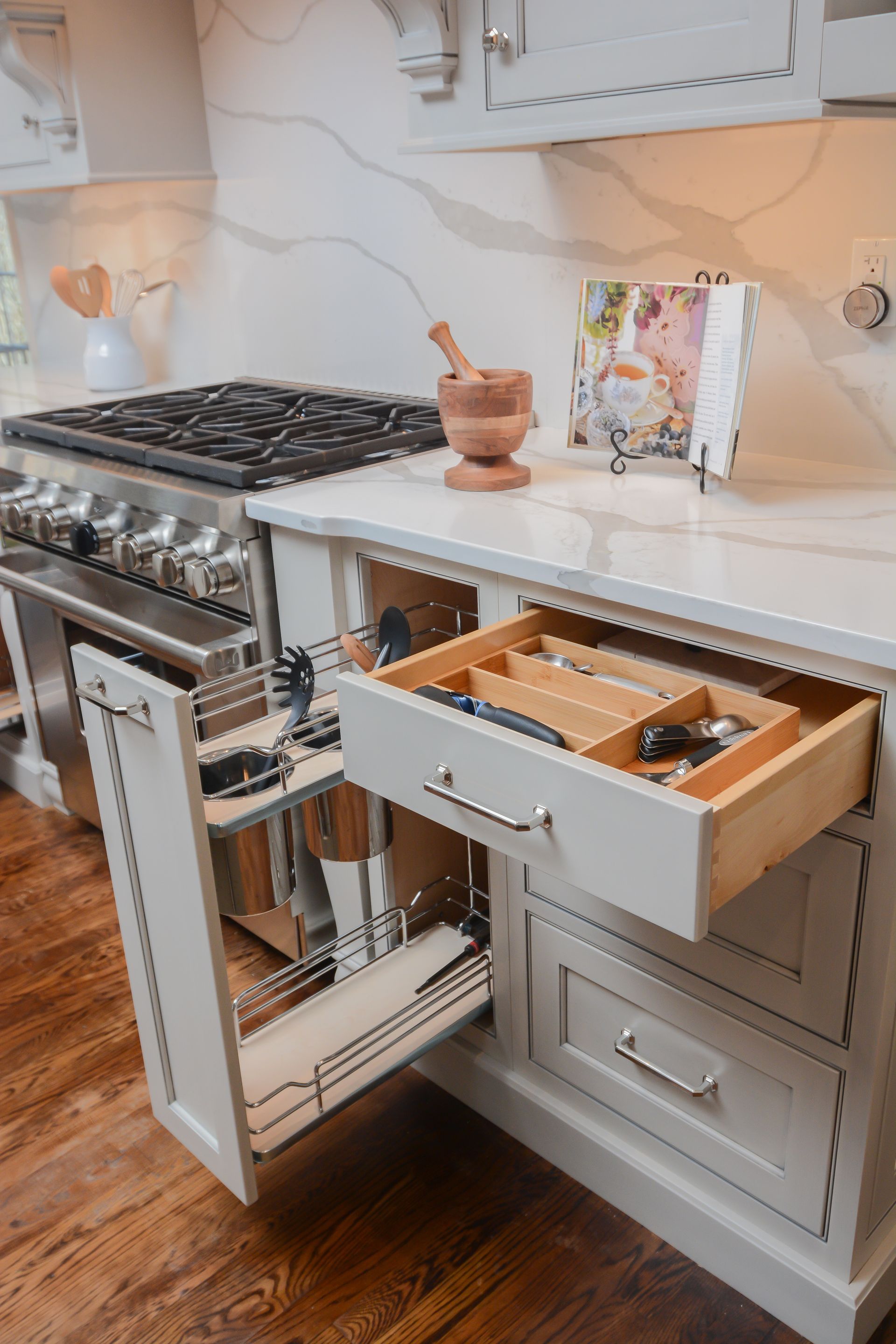Modern kitchen with a stainless steel range and an open drawer of utensils beside a white countertop