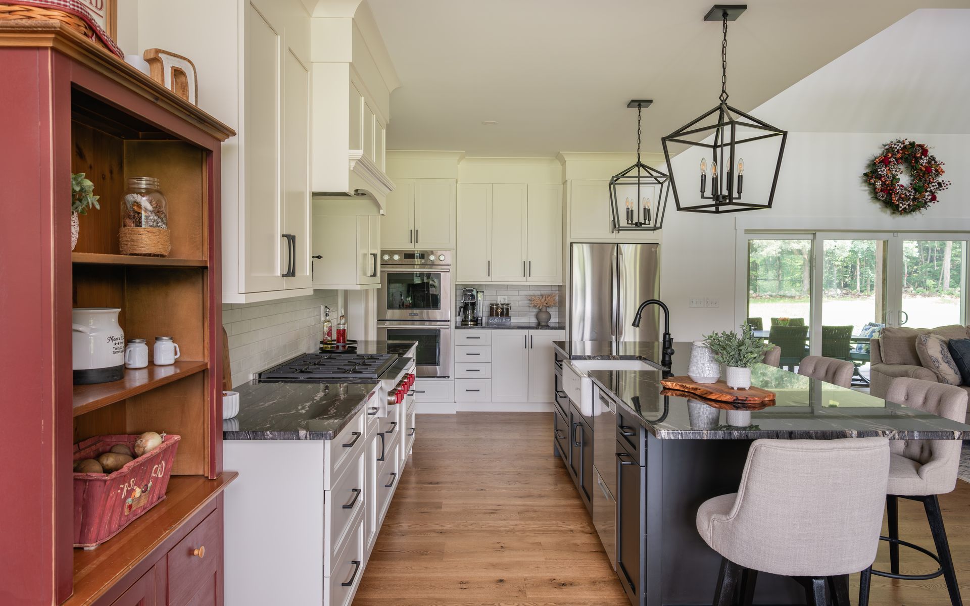 Bright modern kitchen with white cabinets, island seating, wood floors, and large windows overlooking greenery