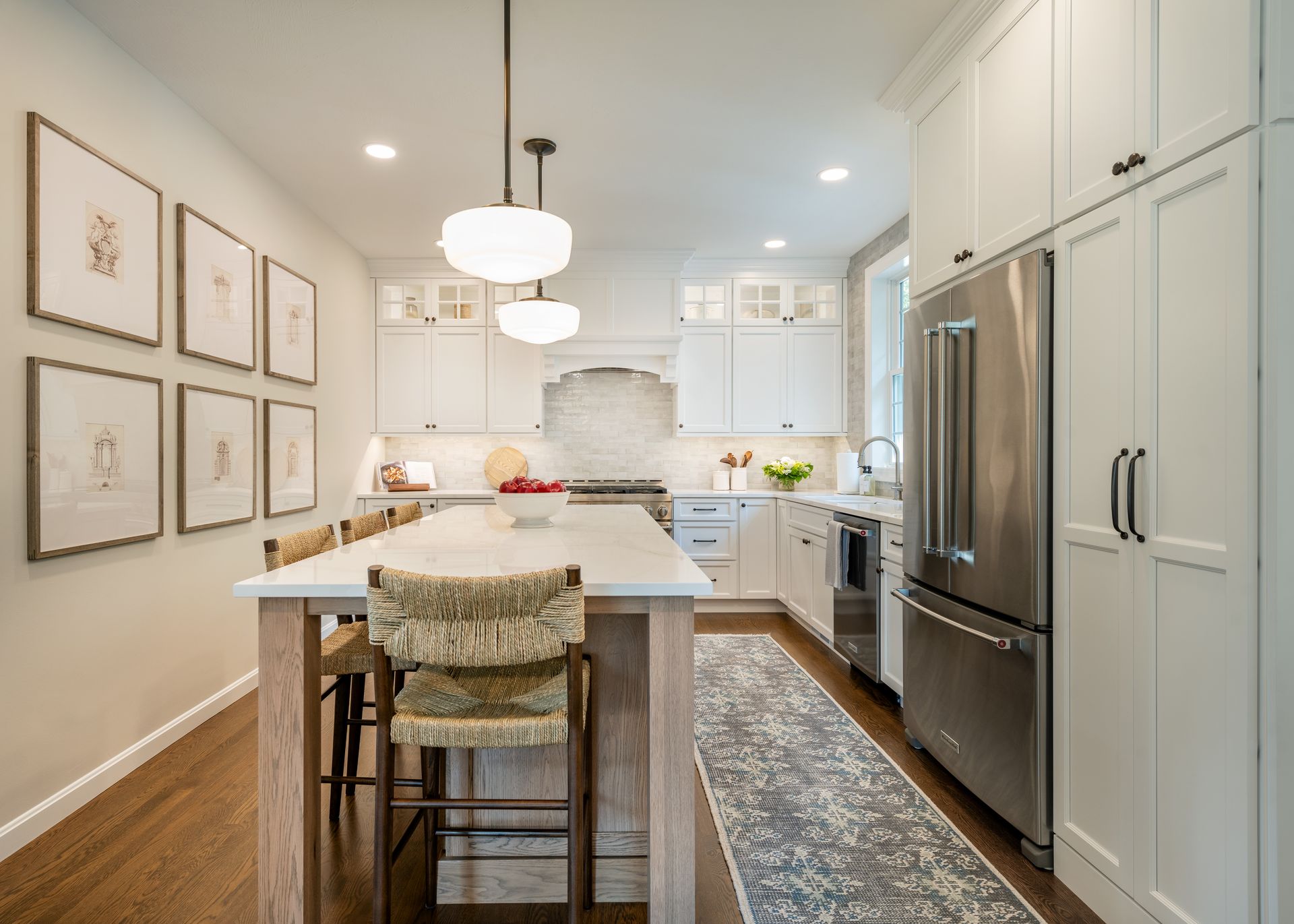 Bright white kitchen with island, stainless steel fridge, pendant lights, and framed wall art.