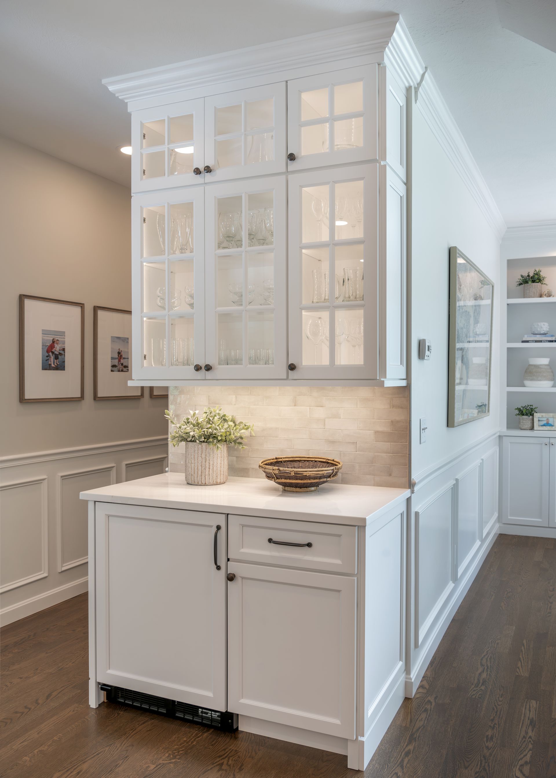 White built-in cabinet with glass upper doors and a small countertop in a bright hallway
