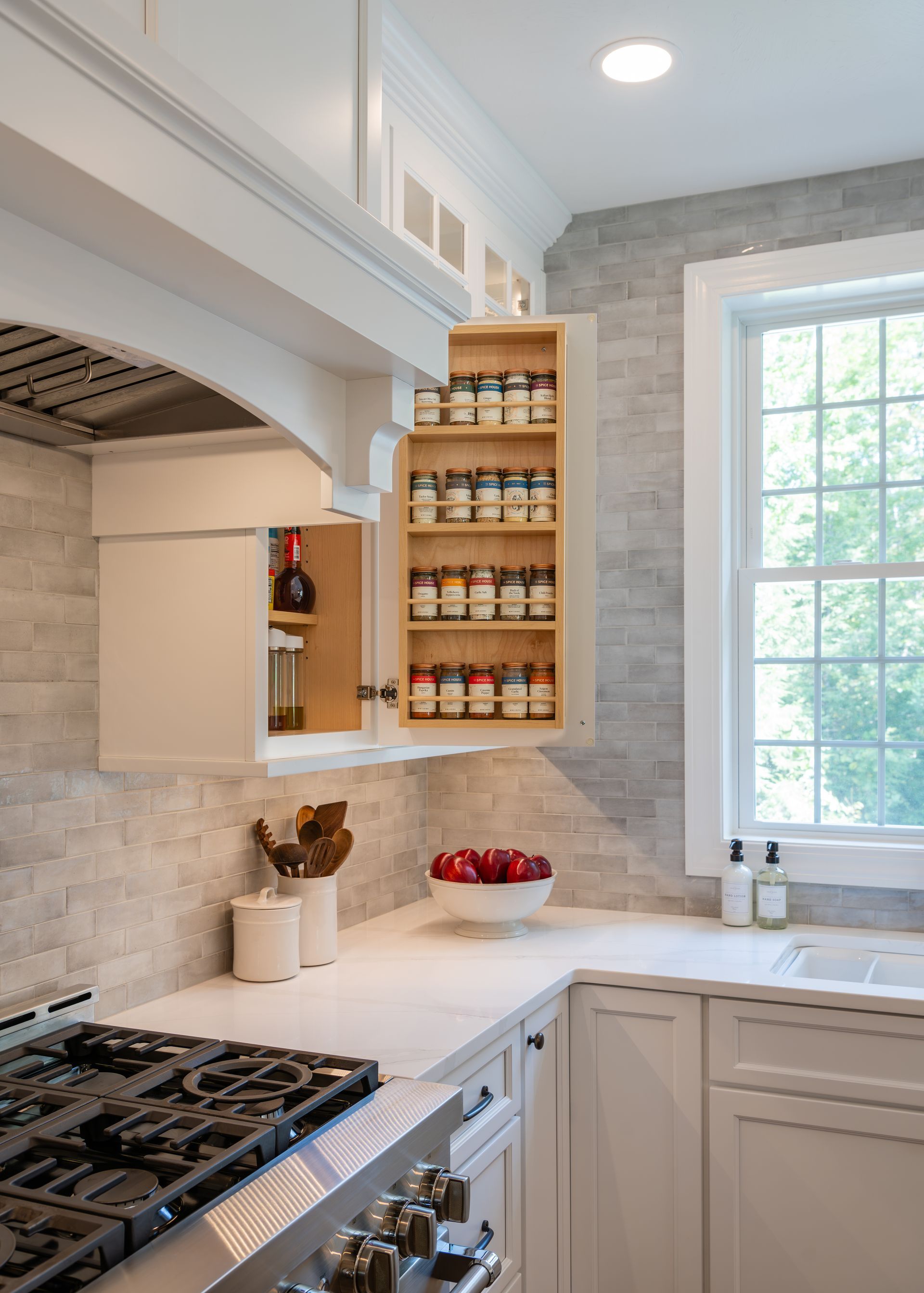 Bright kitchen corner with stove, white counters, open spice shelves, and a large window.