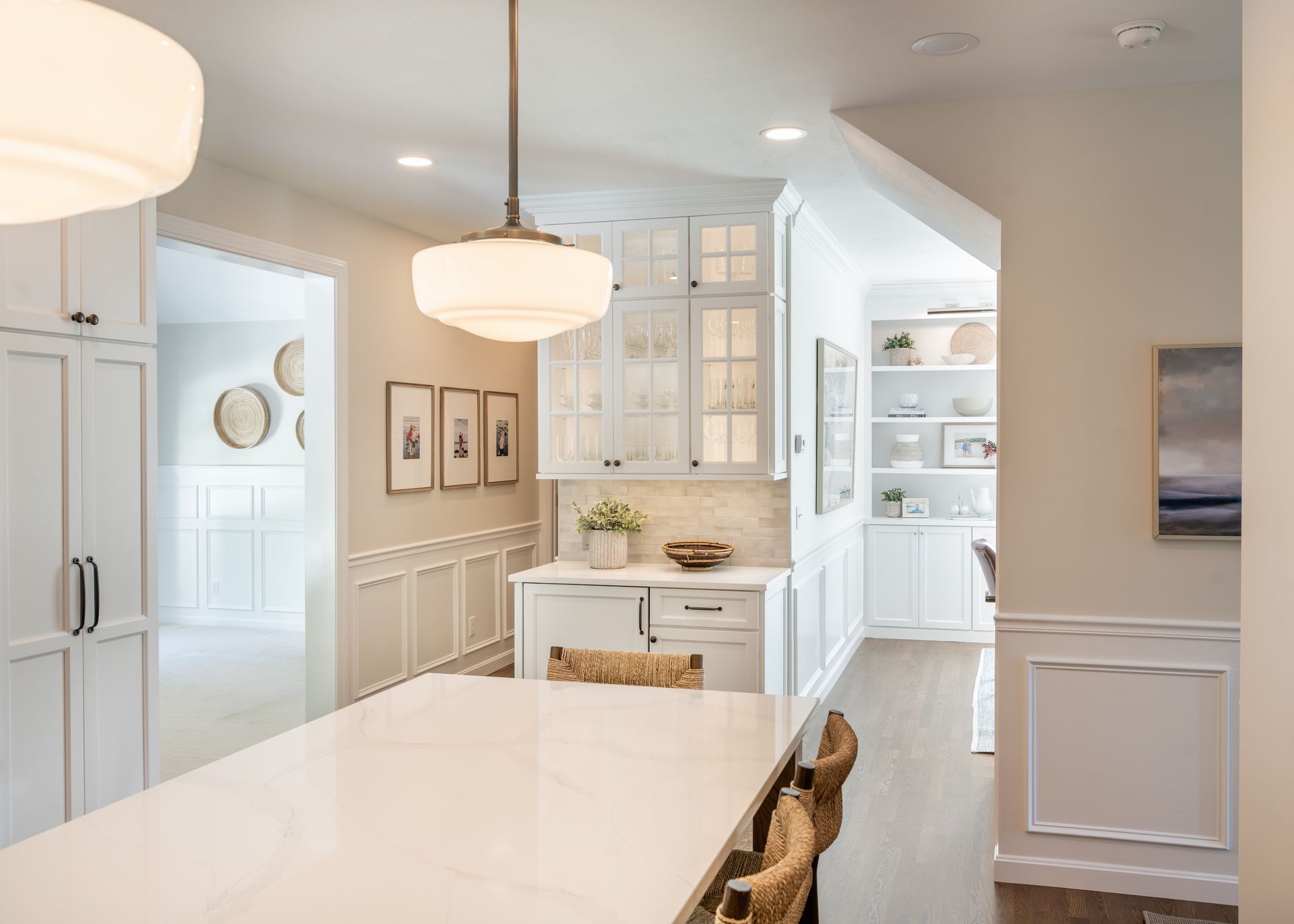 Bright modern kitchen with white cabinetry, marble island, pendant lights, and built-in storage alcove