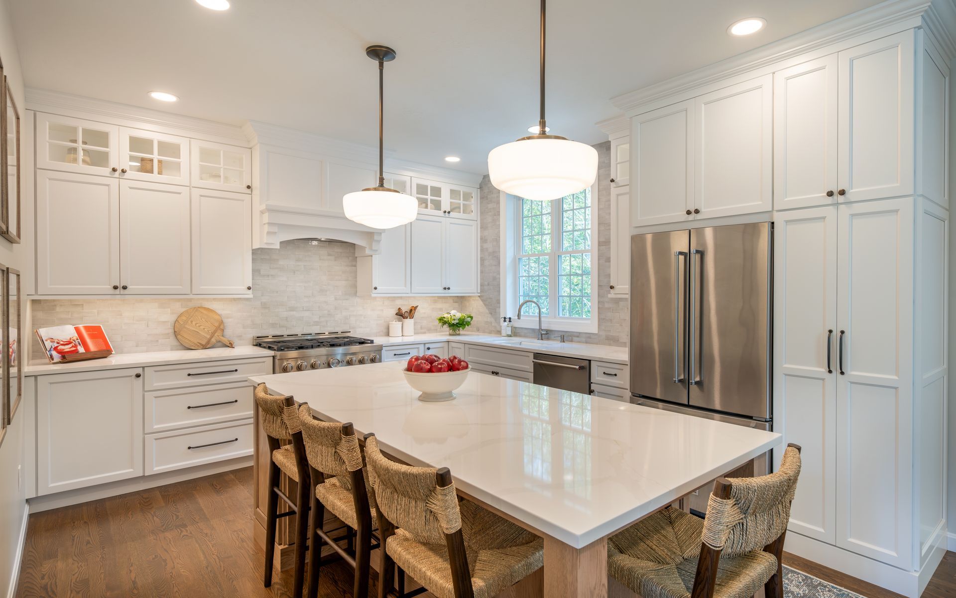 Bright white kitchen with large island, pendant lights, stainless steel fridge, and wood stools