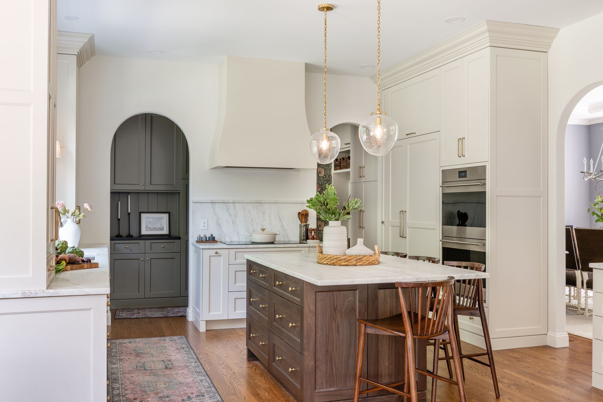 Bright white kitchen with a dark wood island, pendant lights, stools, and arched doorway