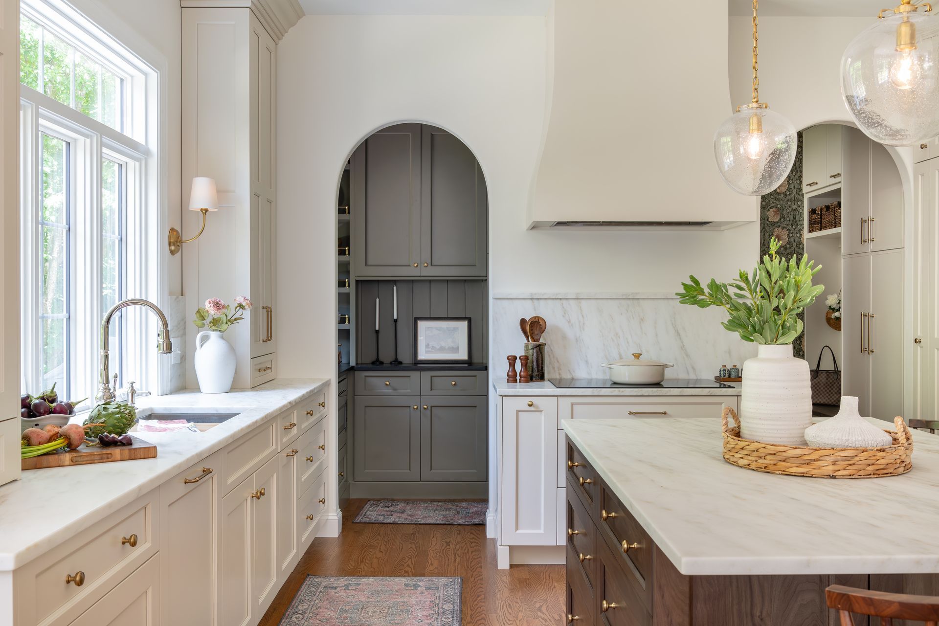 Bright white kitchen with marble island, arched doorway, and green plant centerpiece