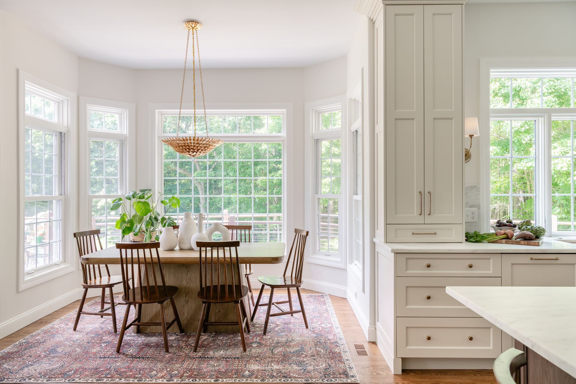 Bright white dining room with large windows, a wooden table, chairs, and built-in cabinets