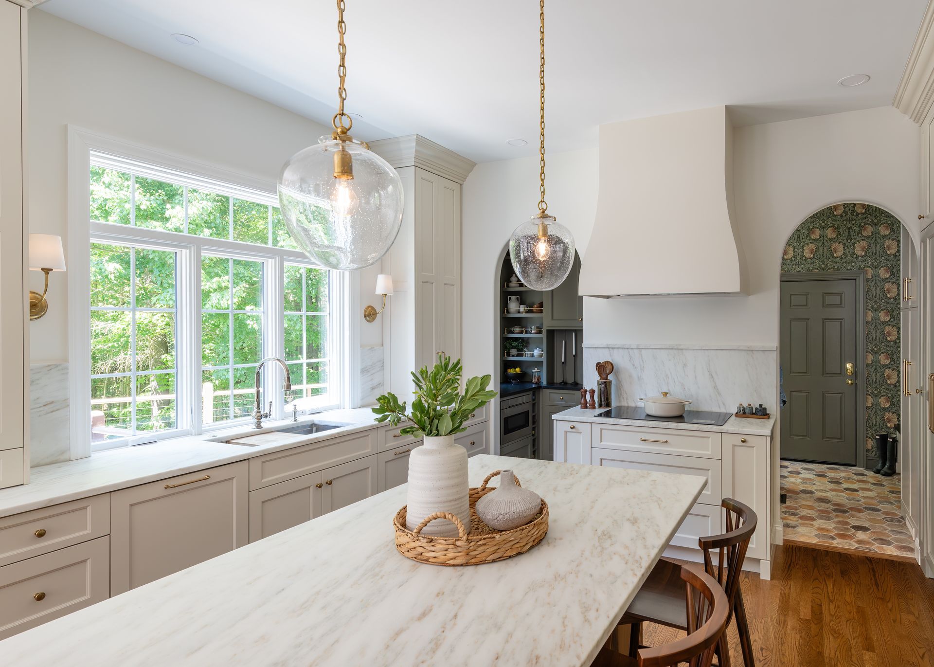 Bright white kitchen with marble island, large windows, pendant lights, and wood floors