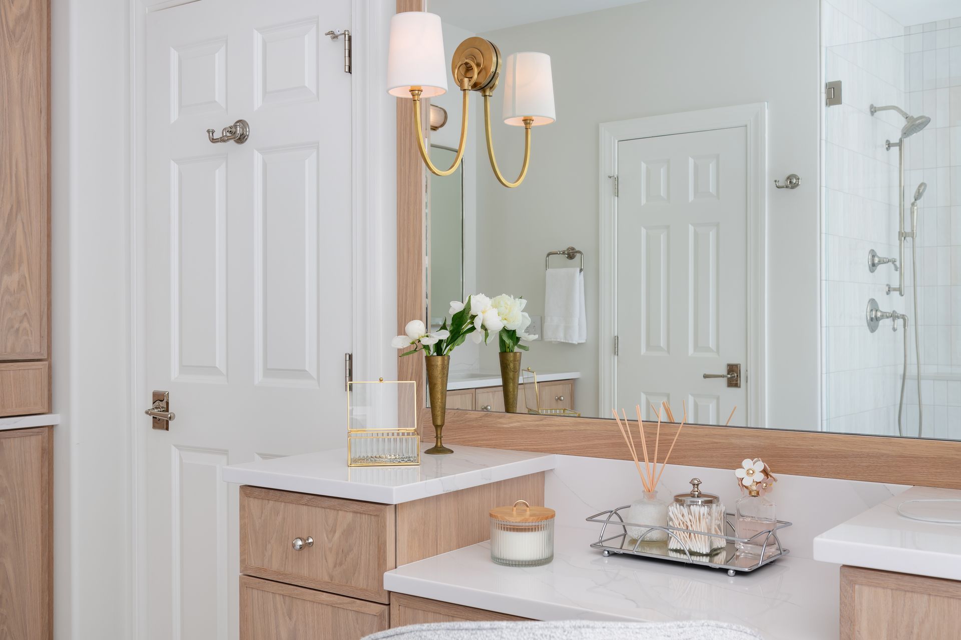 Bright bathroom vanity with gold sconces, white cabinets, mirror, flowers, and toiletries