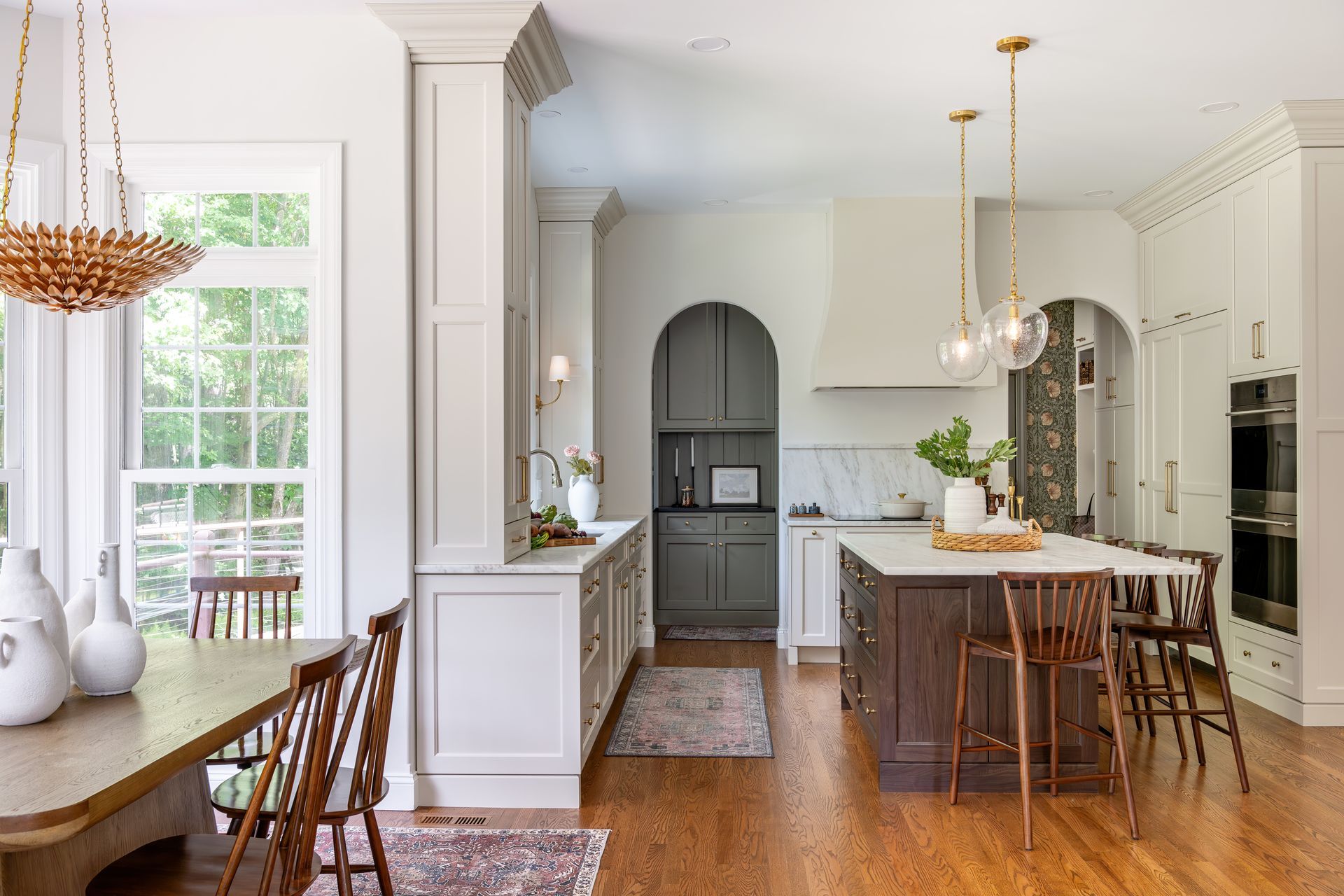 Bright, elegant kitchen with white cabinets, wood floors, island seating, and adjacent dining area