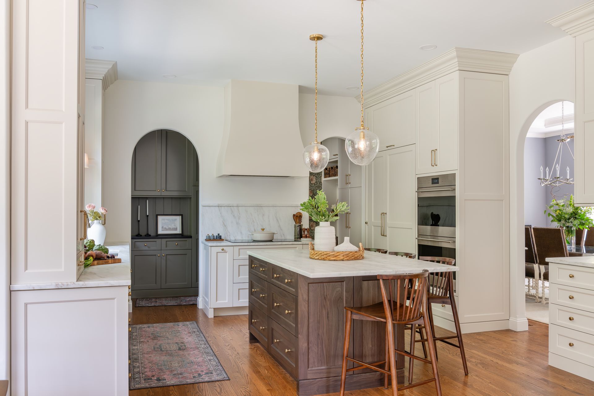 Bright white kitchen with marble island, wood floor, pendant lights, and arched doorway