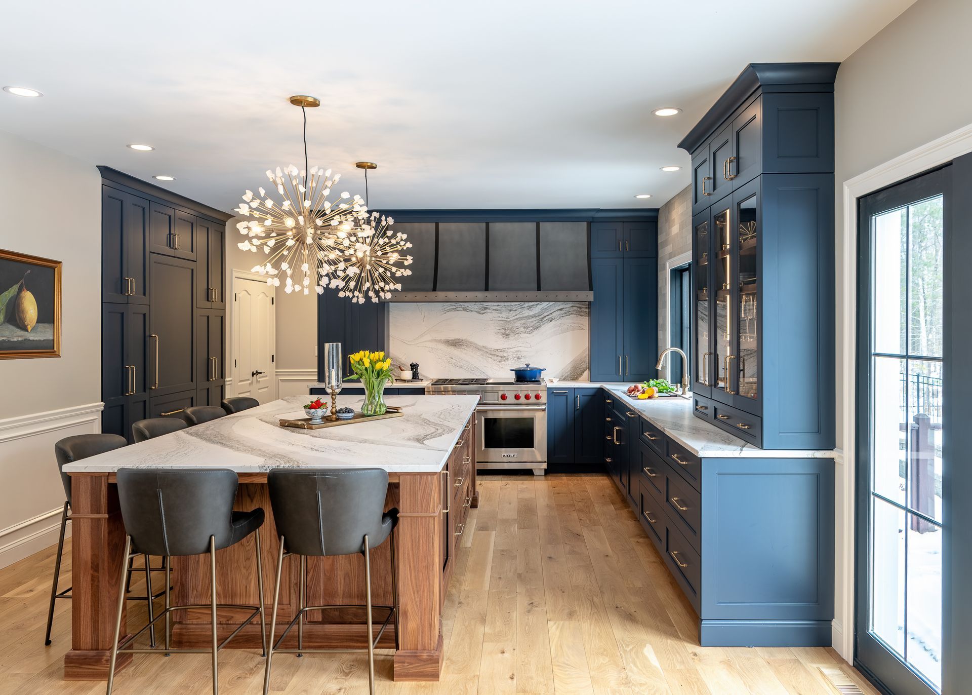 Modern kitchen with blue cabinetry, marble island, chandelier, and large windows on hardwood floors