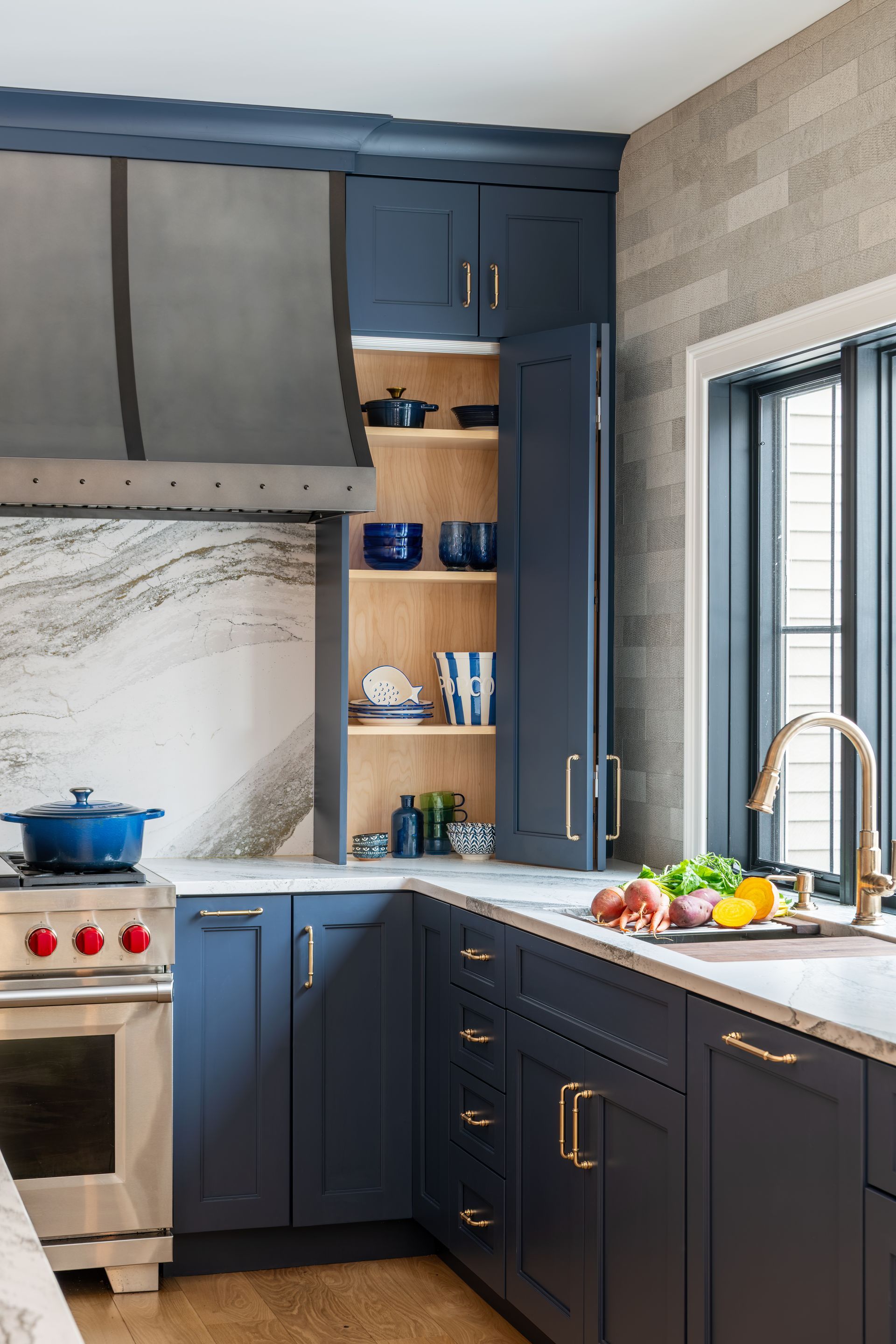 Modern kitchen with navy cabinets, marble counters, open shelves, and a sink by a window