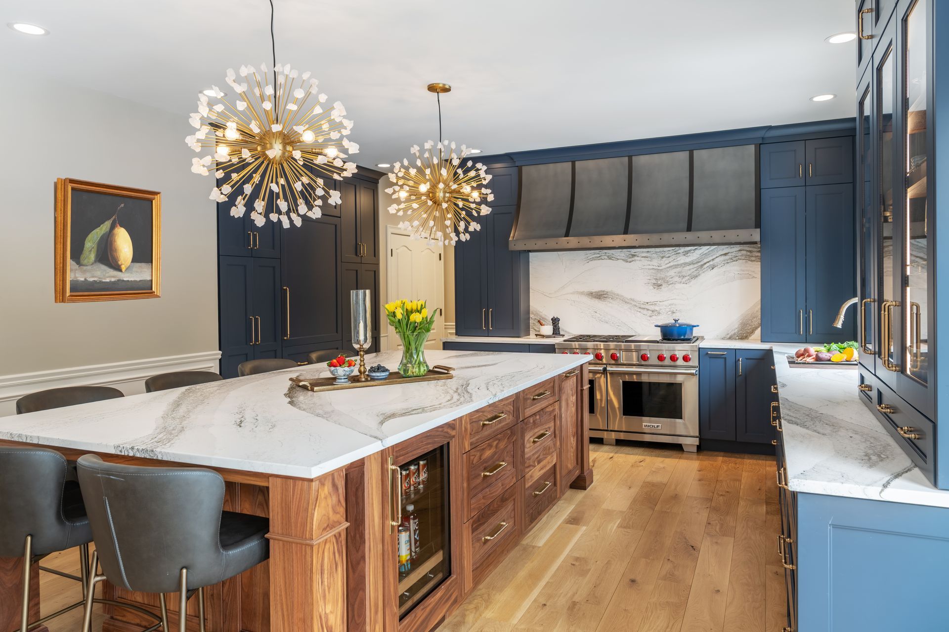 Modern kitchen with navy cabinets, marble island, wood floors, and gold pendant lights