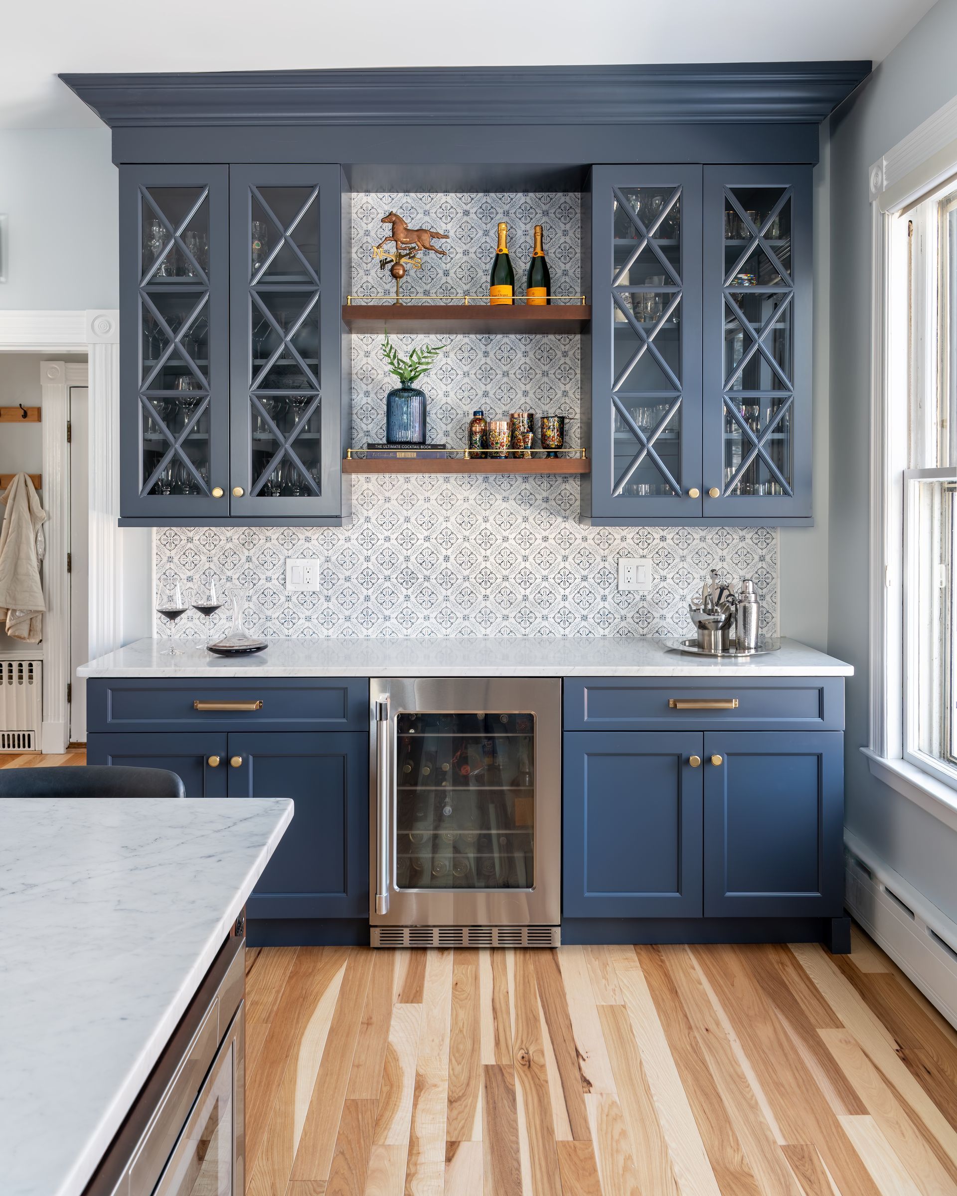 Blue kitchen cabinets with open shelves, marble backsplash, wine fridge, and wood floors.
