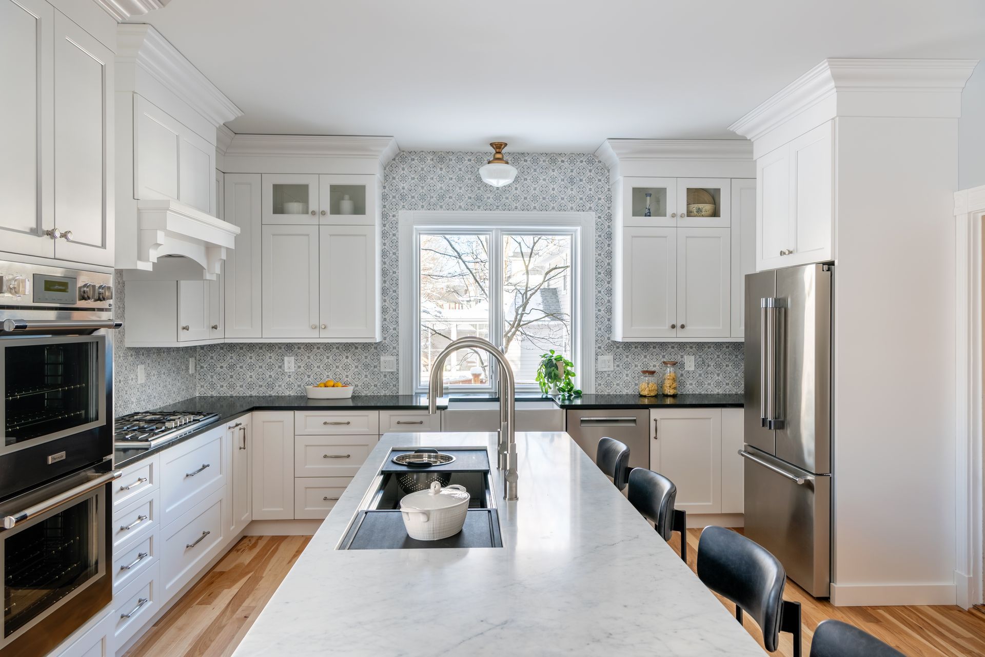 Bright white kitchen with marble island, black stools, and a window over the sink