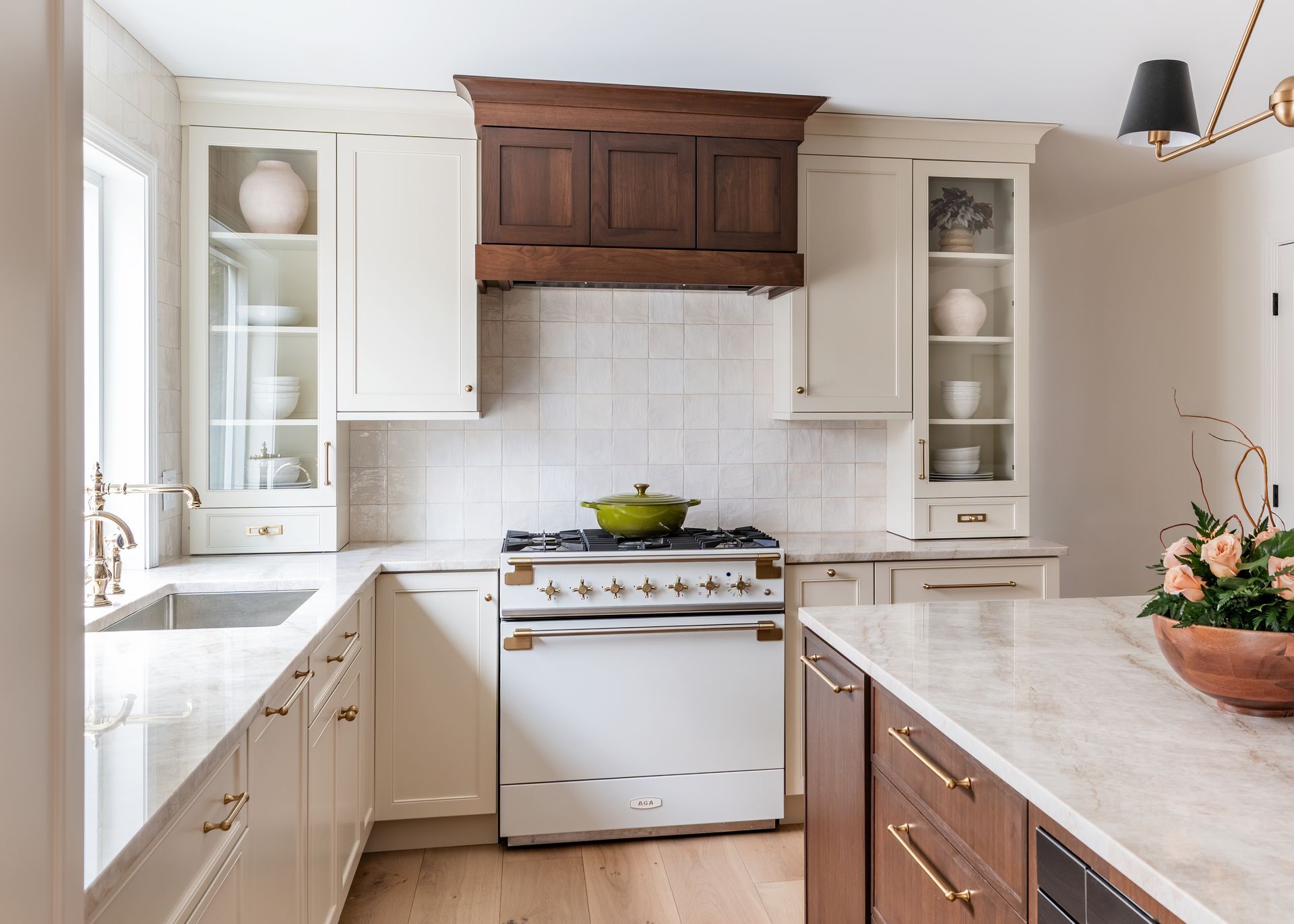Bright kitchen with white cabinets, wood accents, marble counters, and a stainless stove centered under a range hood