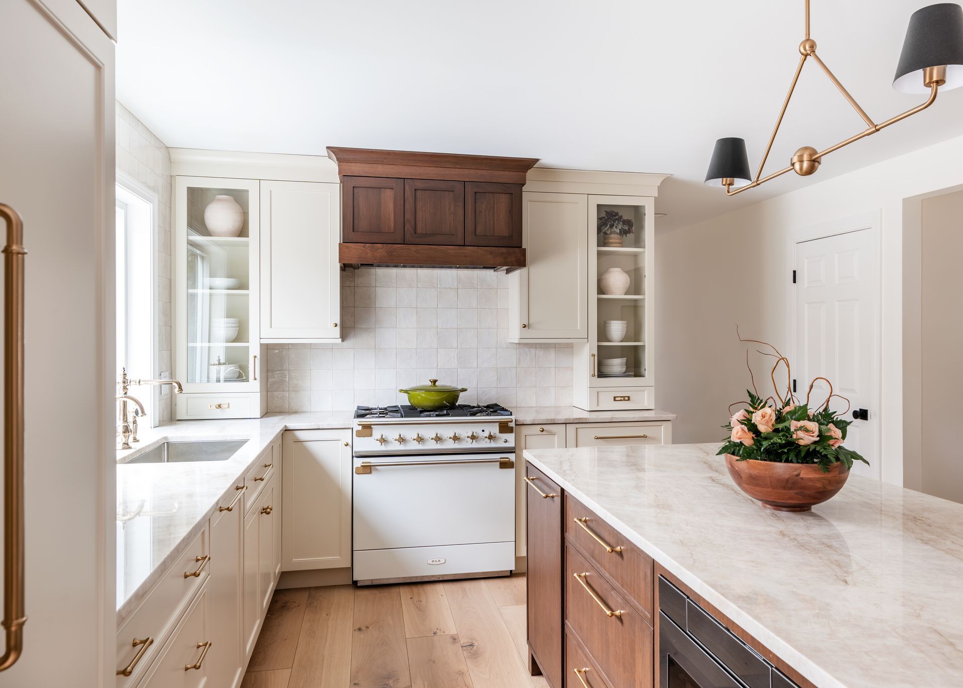 Bright white kitchen with wood cabinets, marble counters, a gas stove, and a bowl of flowers on the island.