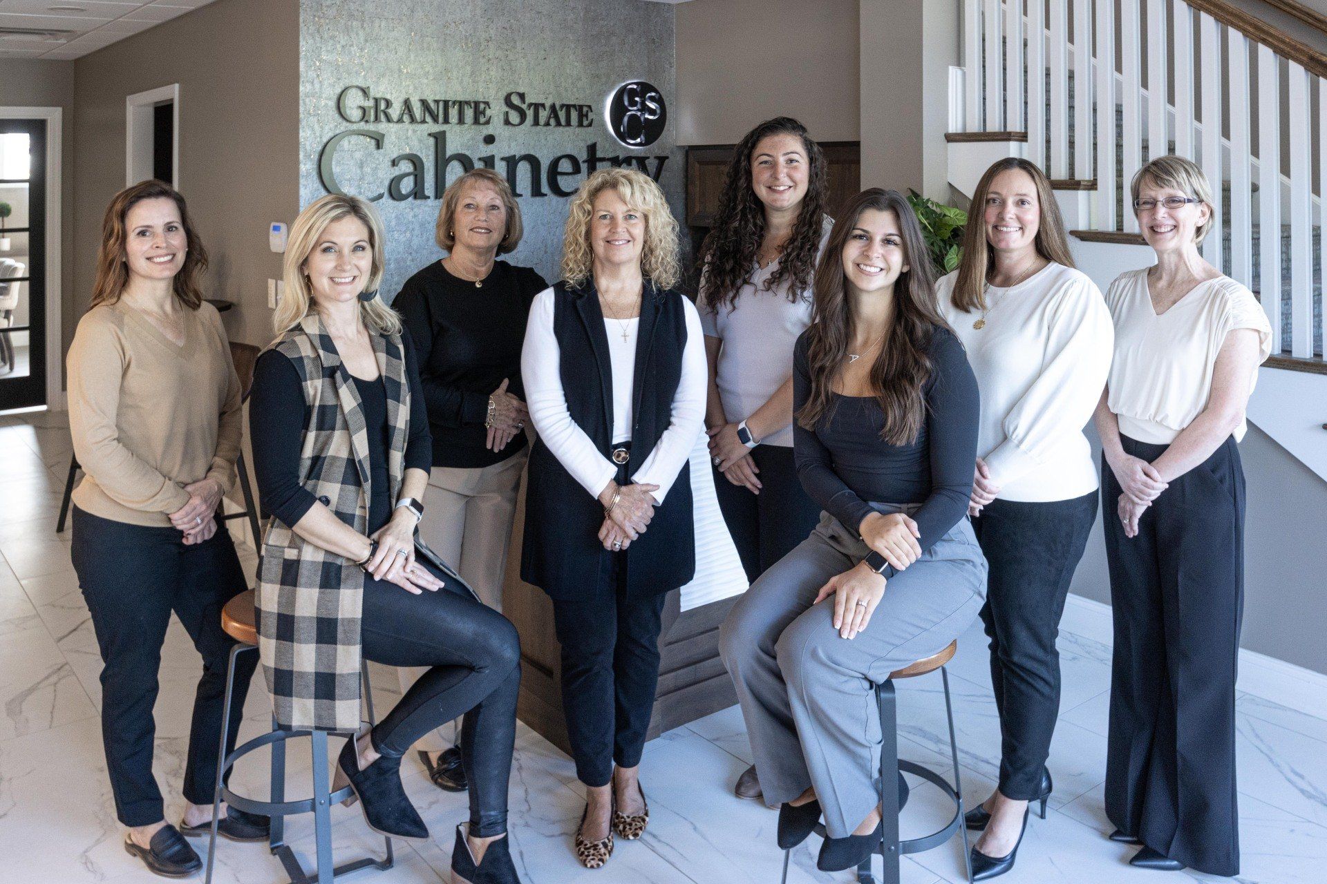 Group of eight people posing in front of a granite state cabinet showroom sign