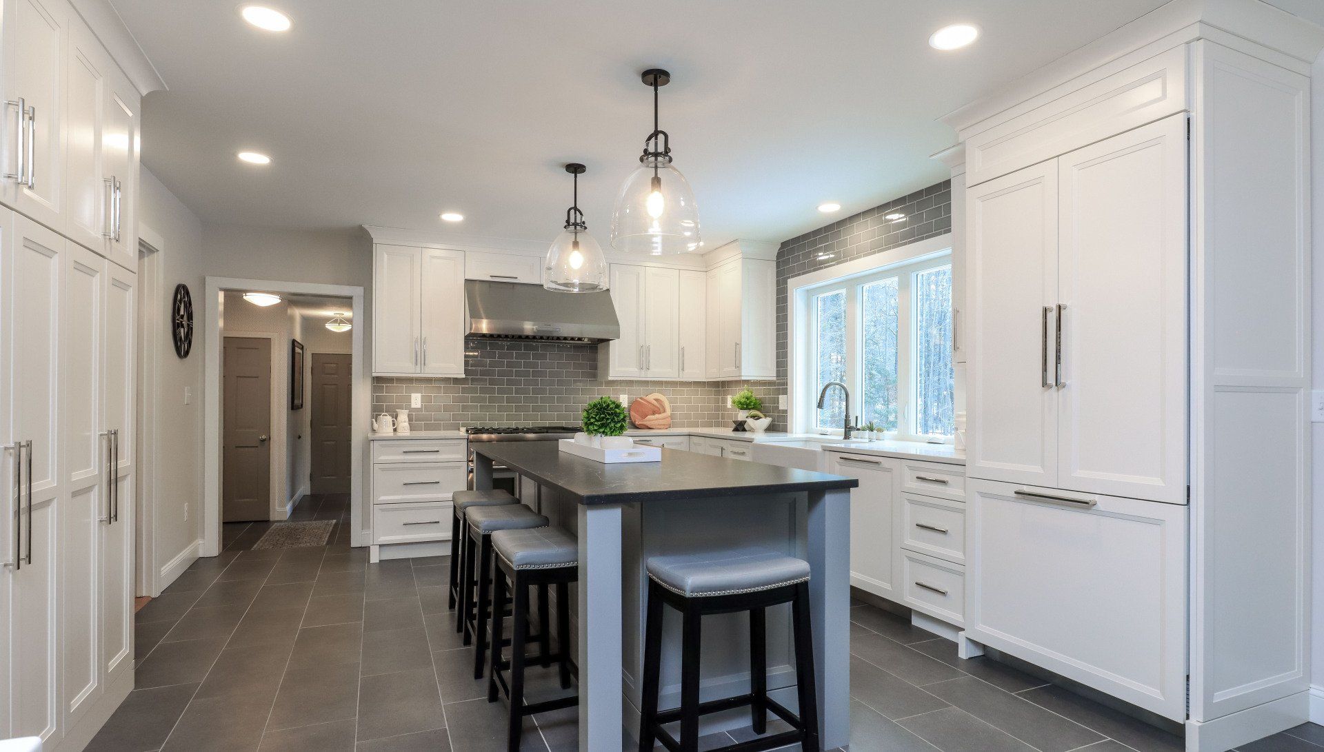 Bright modern kitchen with white cabinets, gray tile floor, island, pendant lights, and bar stools