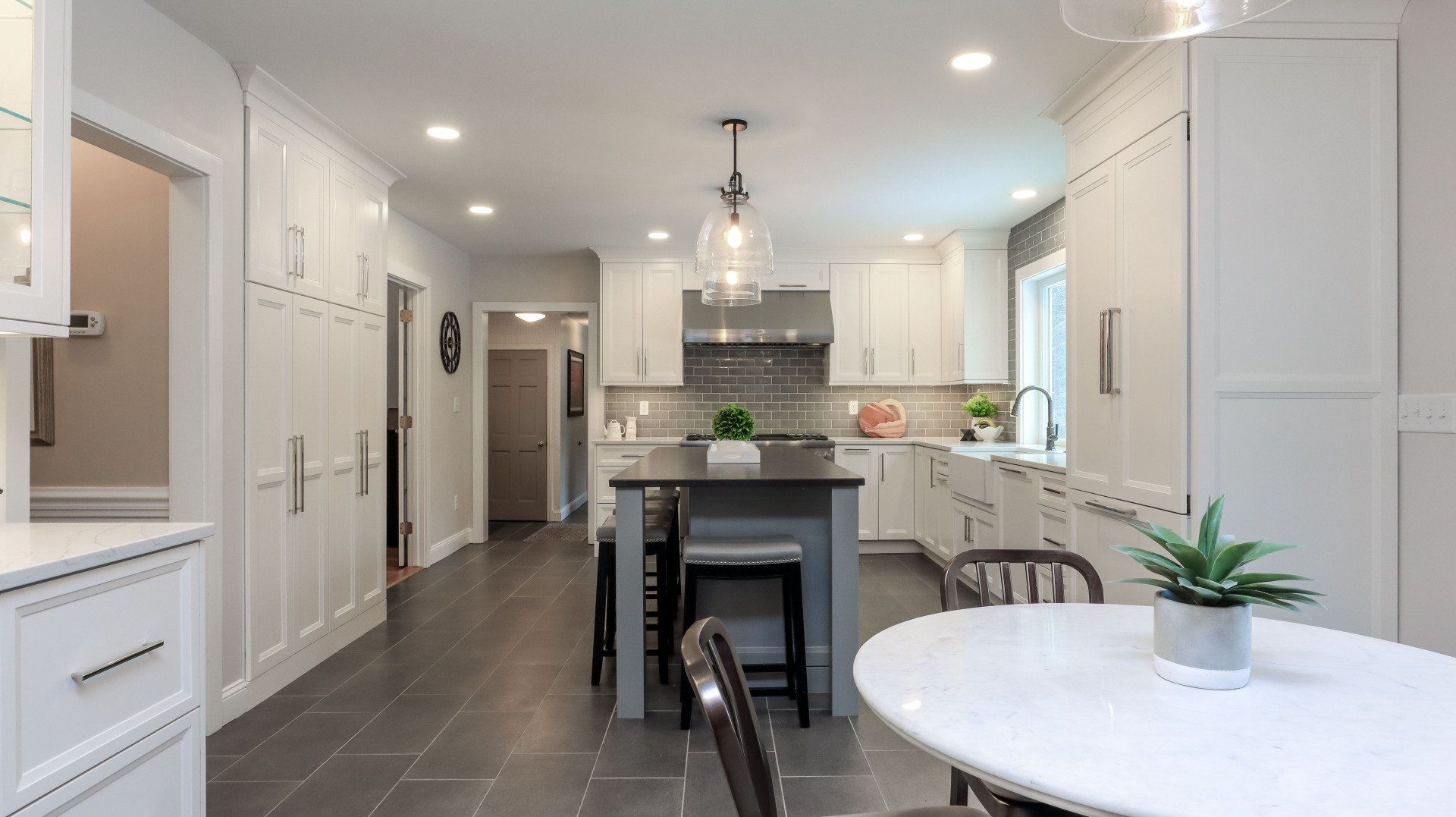 Bright white kitchen with island, gray tile floor, pendant lights, and round dining table by a window