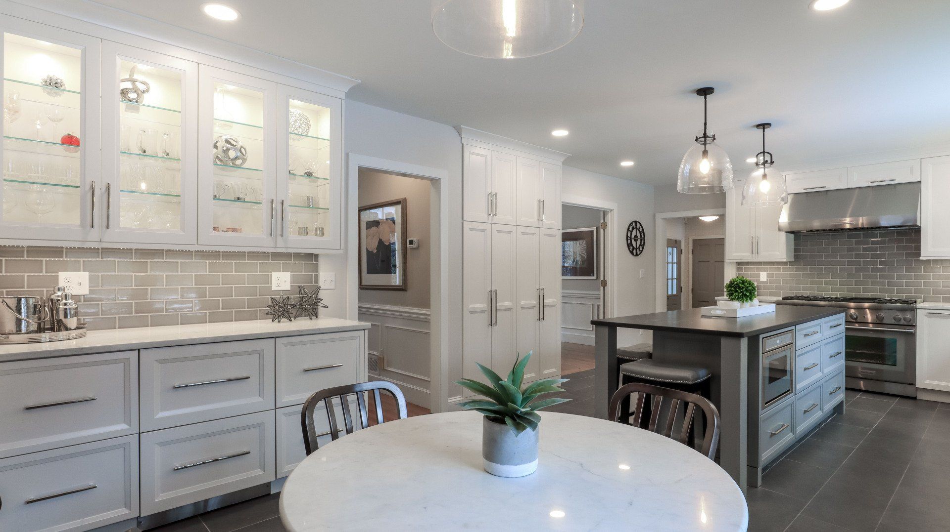 Bright modern kitchen with white cabinets, gray tile, island, and round table with a small plant.