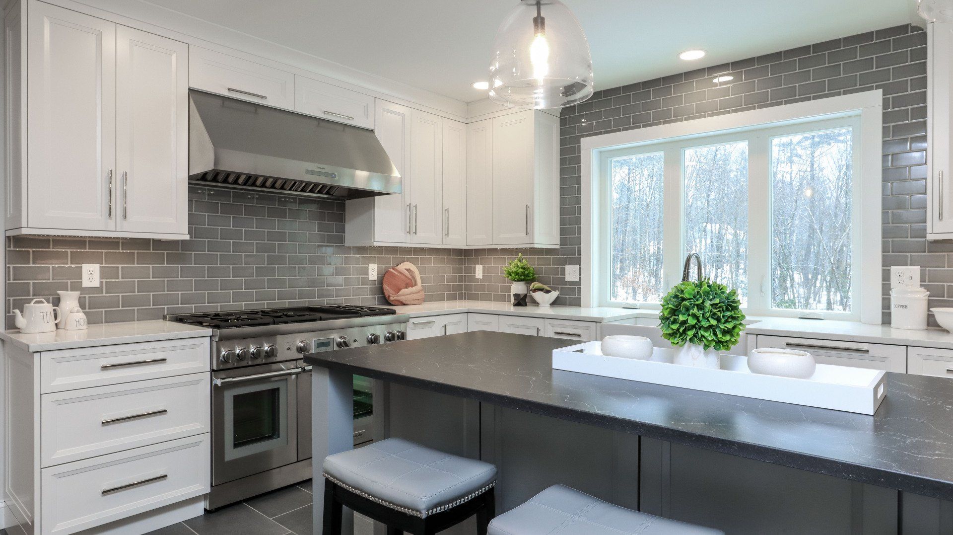 Bright modern kitchen with white cabinets, dark island, stainless appliances, and a window over the sink.