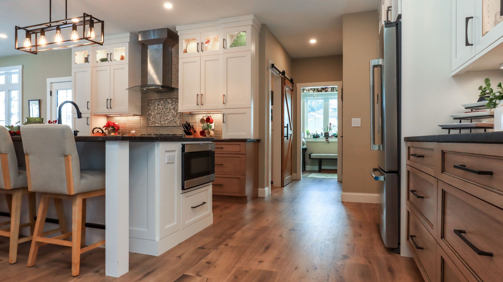 Bright modern kitchen and dining area with white cabinets, wood floors, and a hallway to the back room