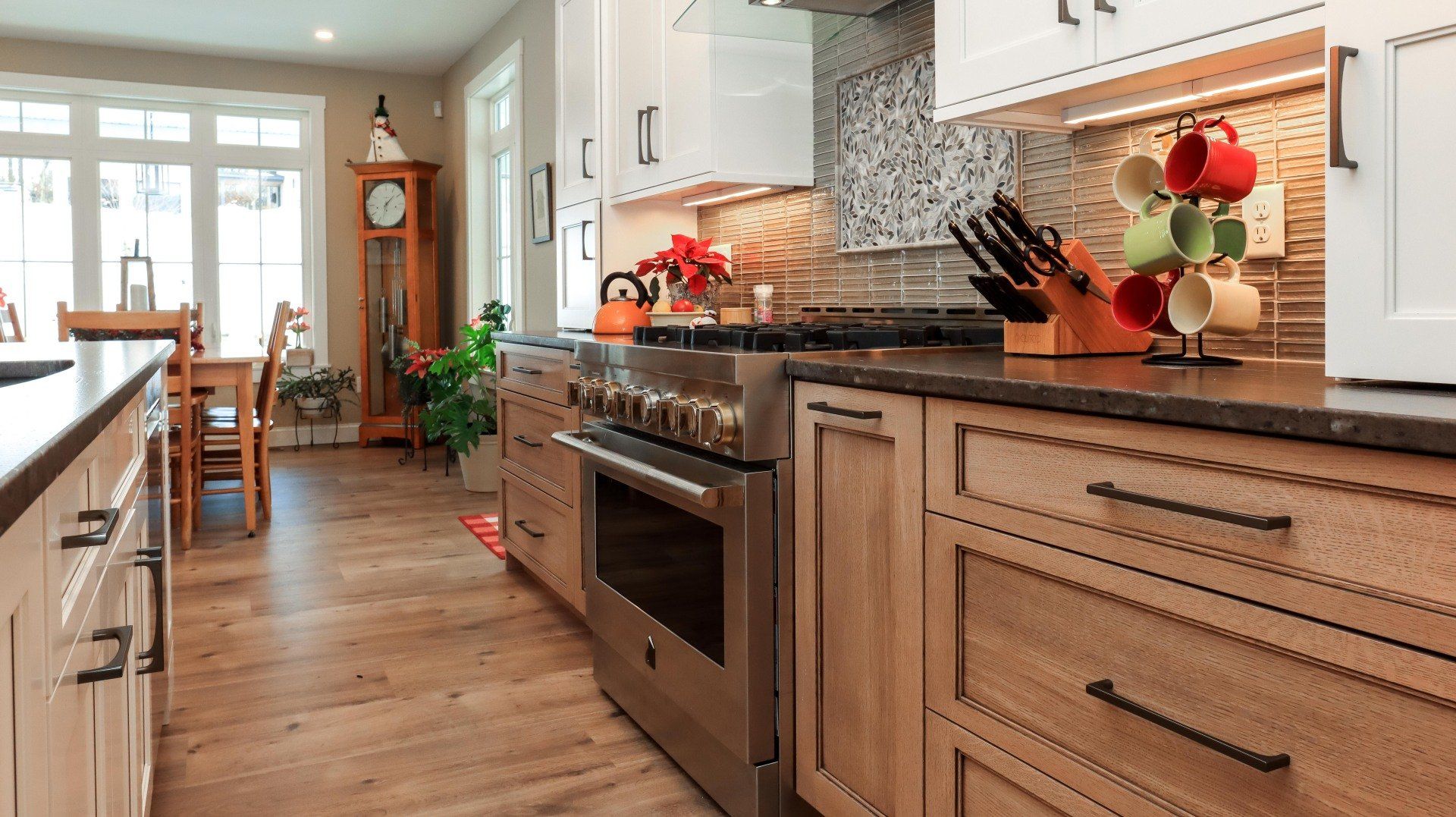Warm modern kitchen with wood cabinets, stainless steel oven, tile backsplash, and a dining area beyond.
