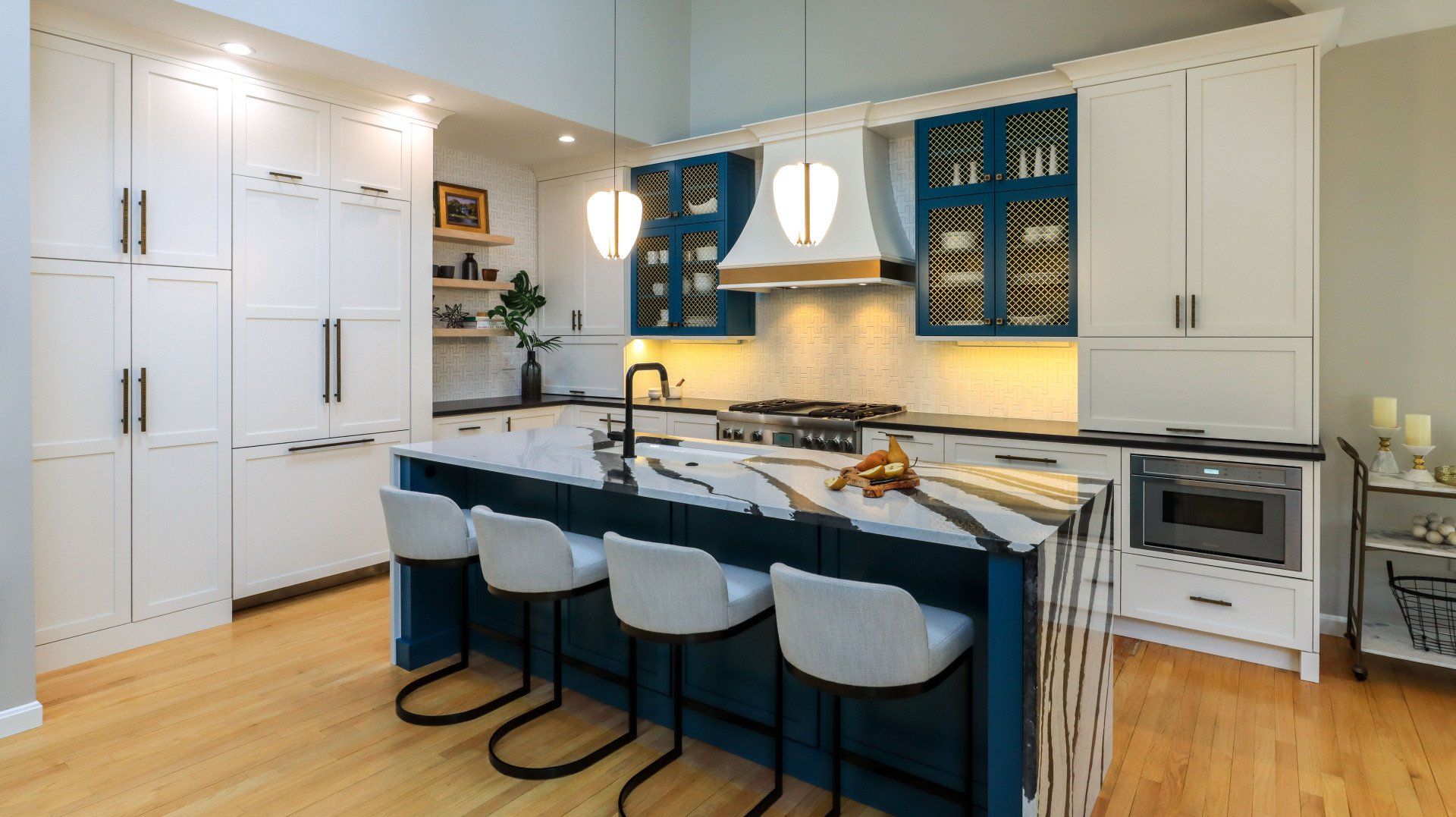 Bright modern kitchen with white cabinets, blue island, and four stools under pendant lights
