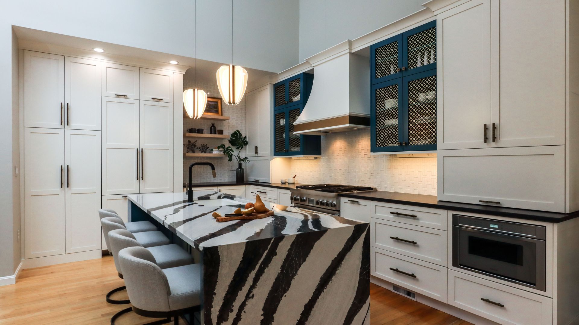 Modern white kitchen with blue accents, island seating, hanging lights, and stainless steel appliances