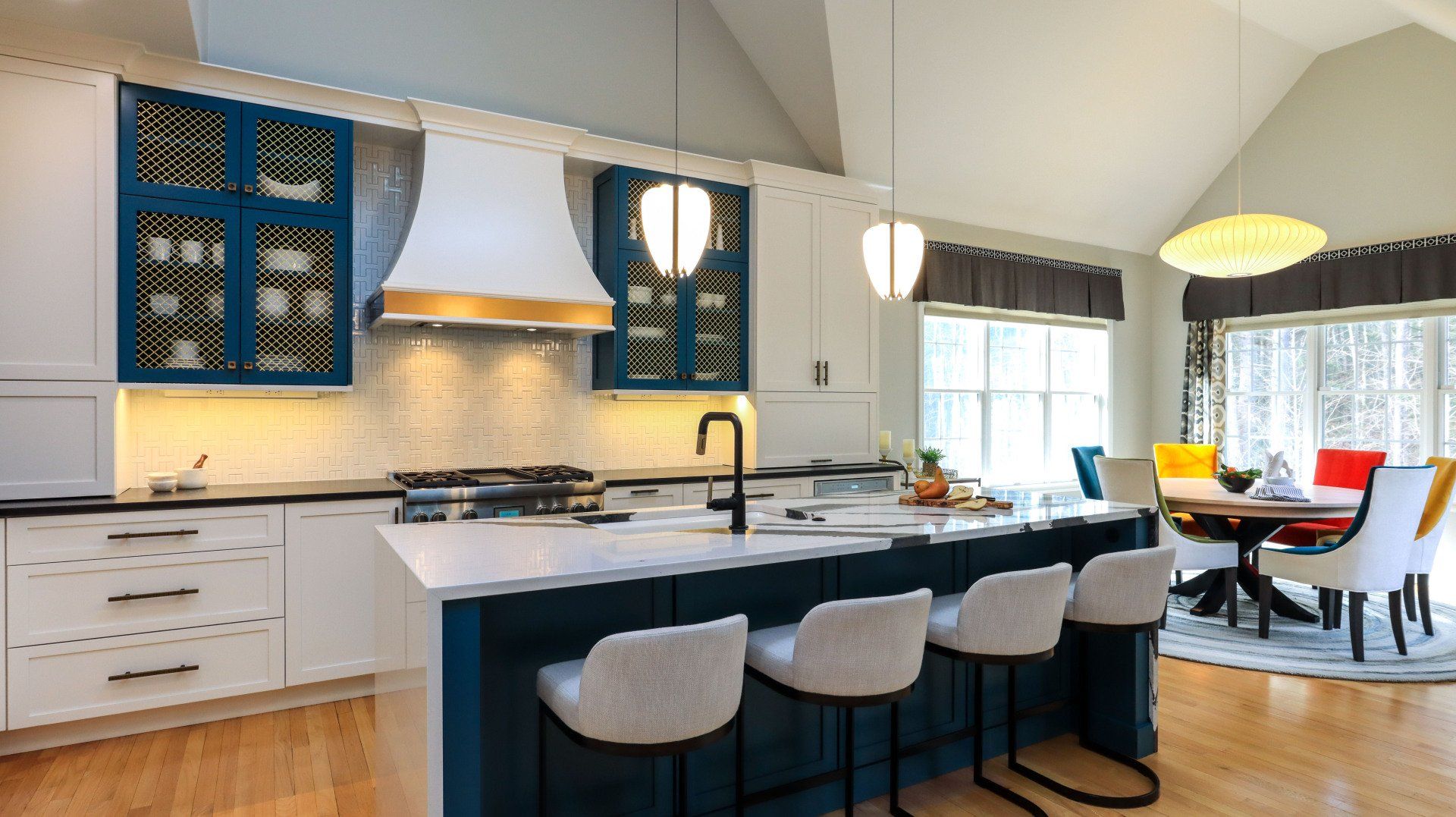 Bright modern kitchen with white cabinets, navy island, pendant lights, and a small dining area by the window