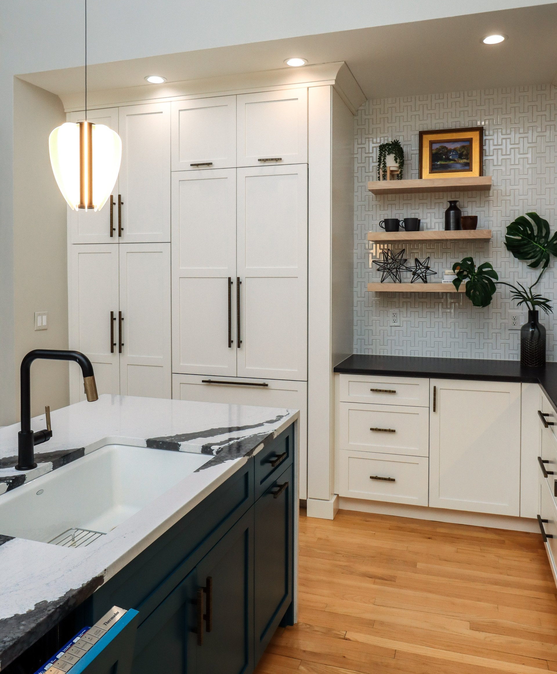 Modern kitchen with white cabinets, black island sink, wood floor, and open shelving on a patterned backsplash.