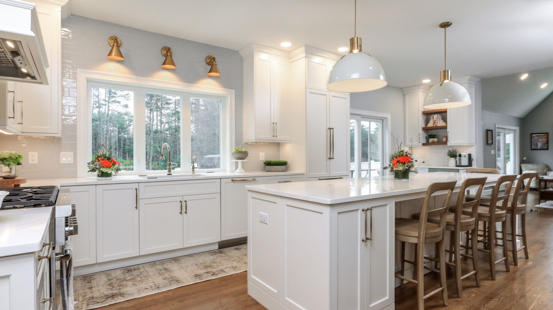Bright white kitchen with island, pendant lights, large windows, and barstools along the counter