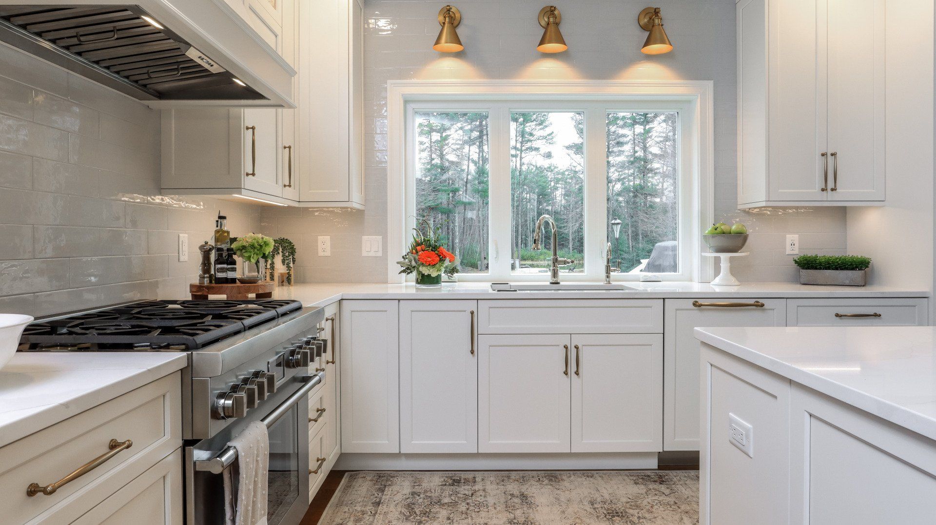 Bright white kitchen with stainless appliances, large window, and small plants on the counter.